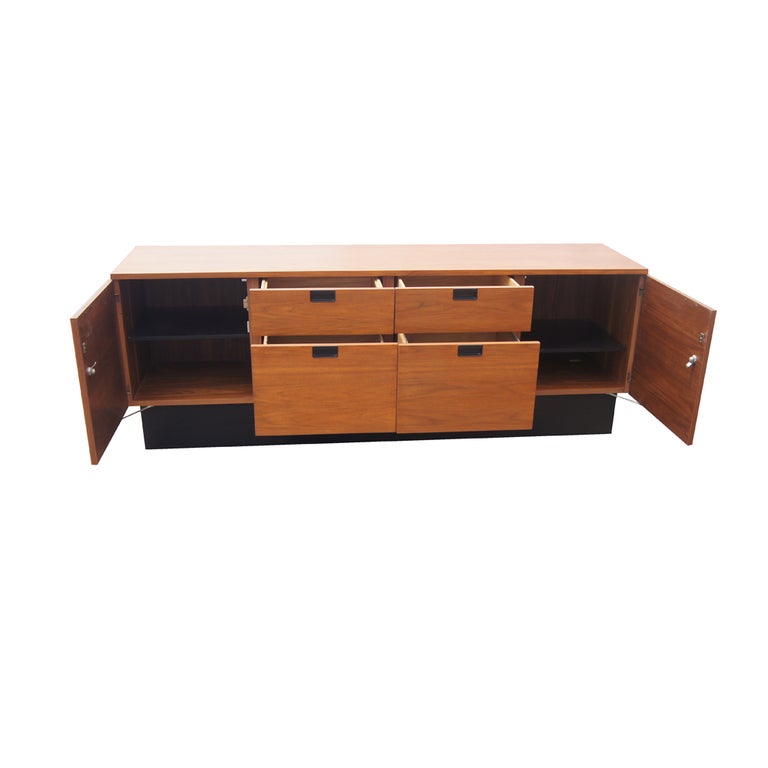 Un aparador moderno de mediados de siglo diseñado por George Nelson y fabricado por Herman Miller. Construcción de nogal con cuatro cajones y dos puertas que ocultan almacenaje en estanterías sobre una base de zócalo negra. Ver escritorio disponible.