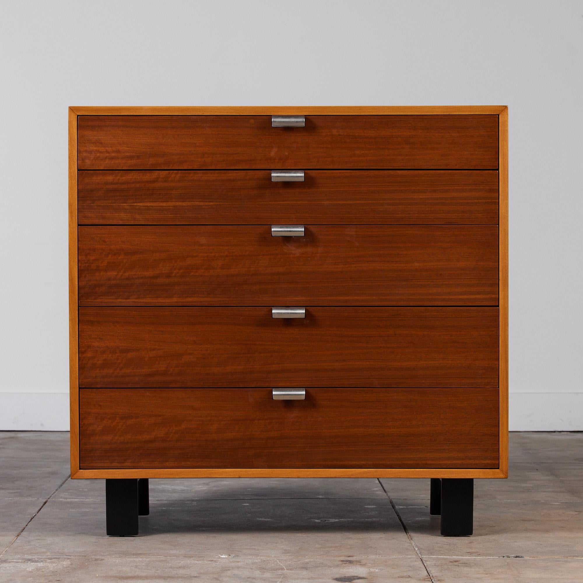 Dresser by George Nelson for Herman Miller, c.1950s. This five-drawer dresser features a walnut frame with sculpted aluminum pulls and sits atop four short plinth black legs. The top drawer features separations for smaller belongings and bears the