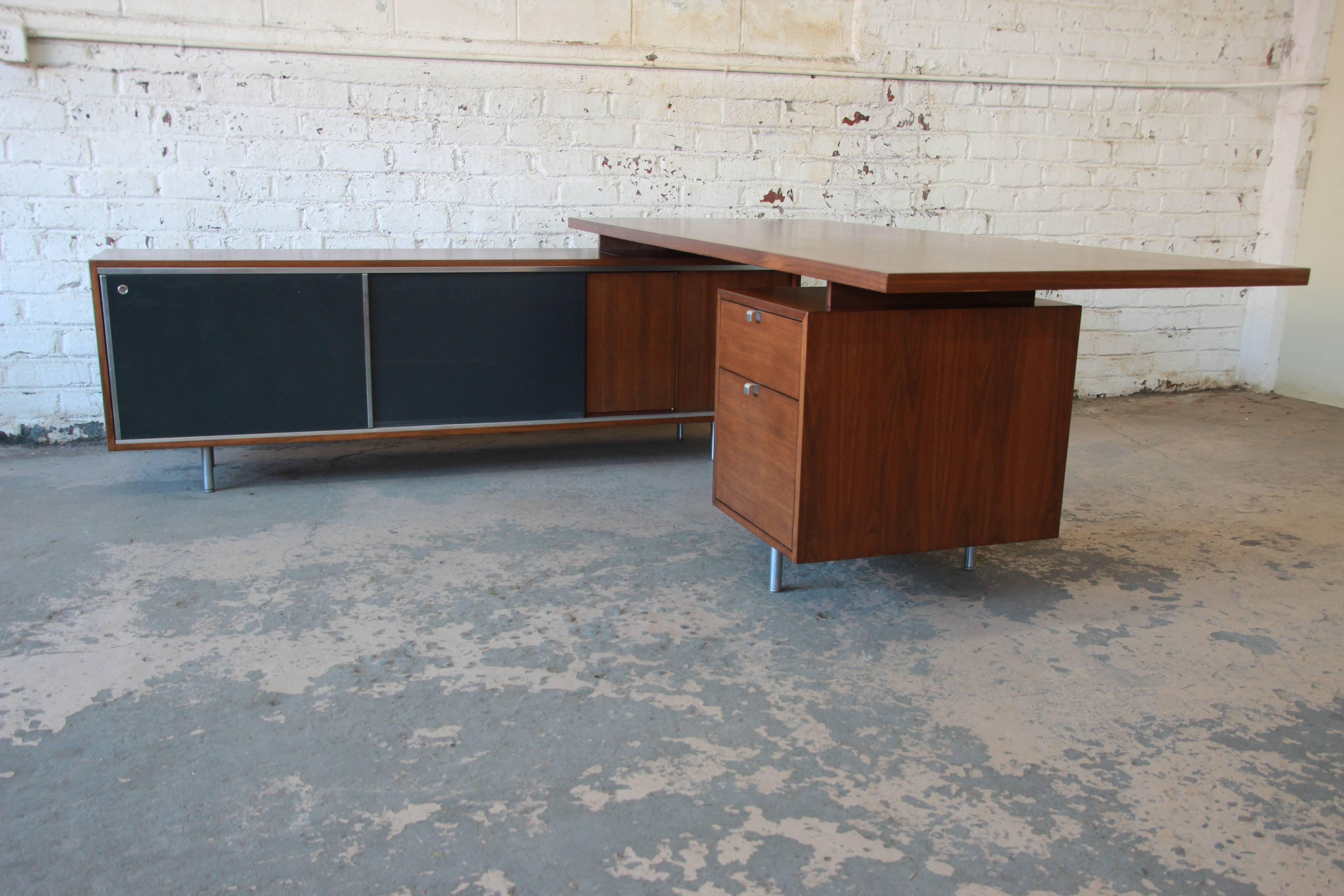 A rare and outstanding Mid-Century Modern L-shaped executive desk designed by George Nelson for Herman Miller. The desk features gorgeous walnut wood grain, with sleek metal feet and hardware. The credenza offers ample room for storage with five
