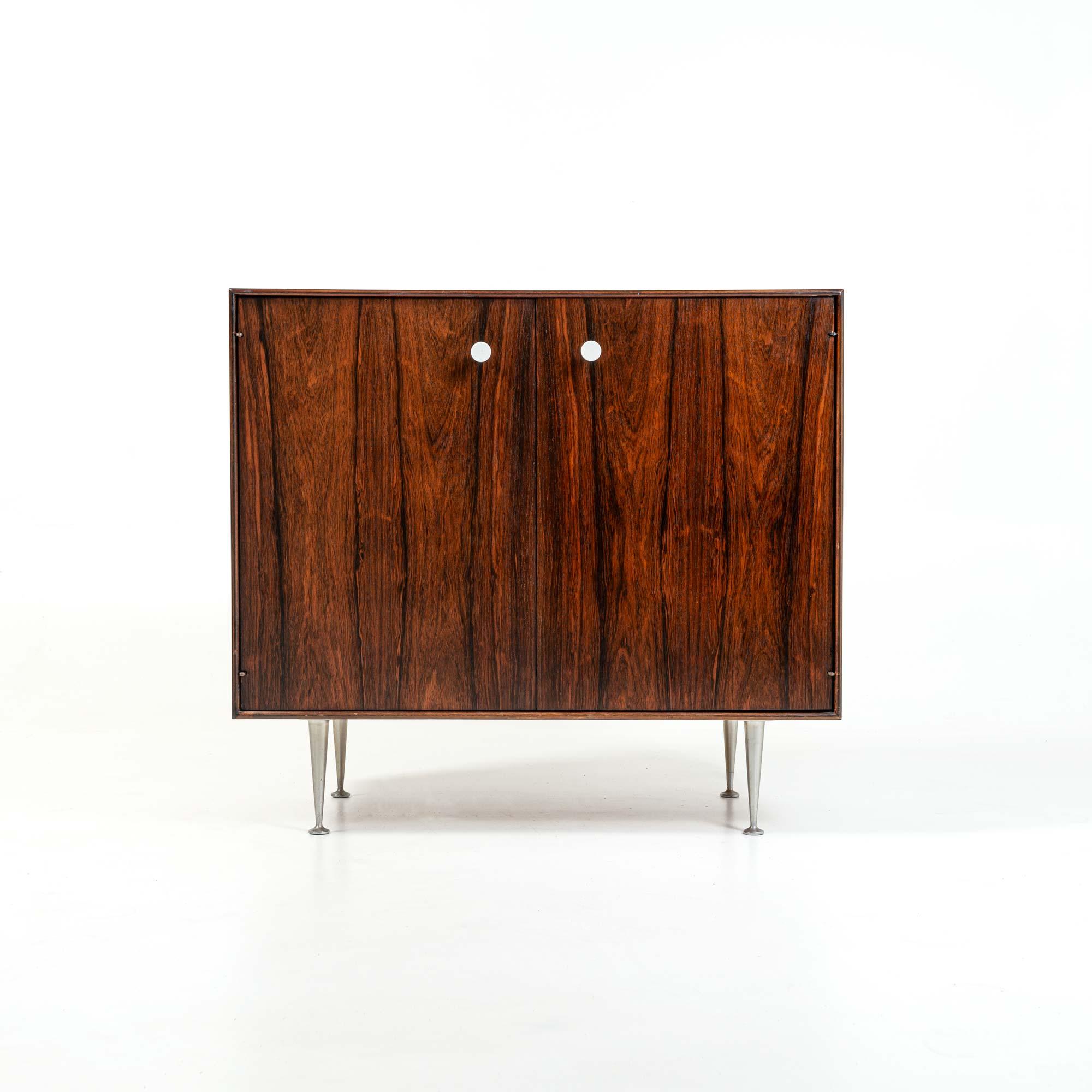An two door designed by George Nelson for Herman Miller, in Brazilian rosewood with its original white porcelain pulls and classic Thin Edge aluminum legs. The cabinet has one inner adjustable shelf. The doors have great graining inside and outside.