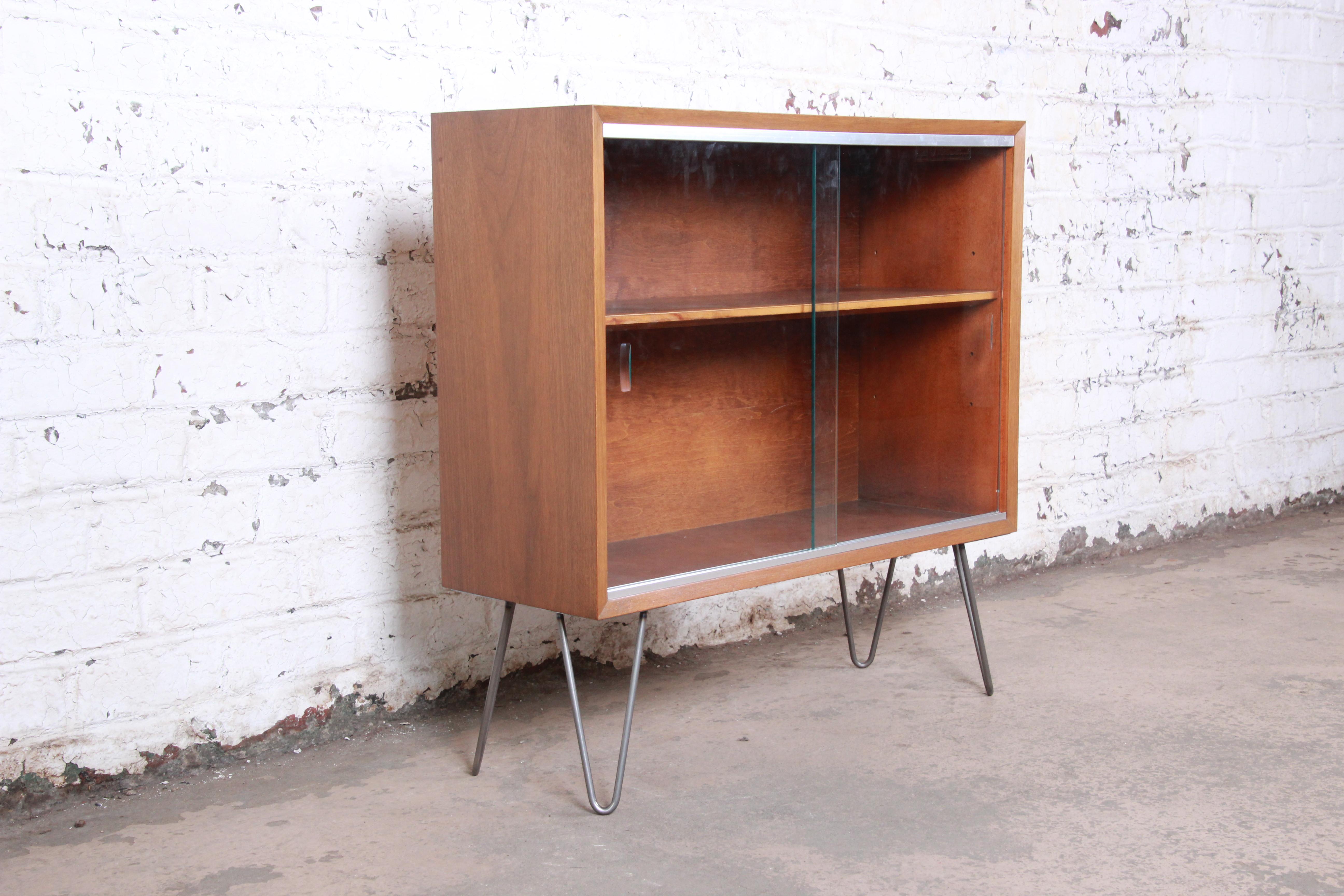 A sleek Minimalist Mid-Century Modern walnut glass front bookcase on hairpin legs

By George Nelson for Herman Miller

USA, circa 1950s

Walnut + glass + steel

Measures: 34