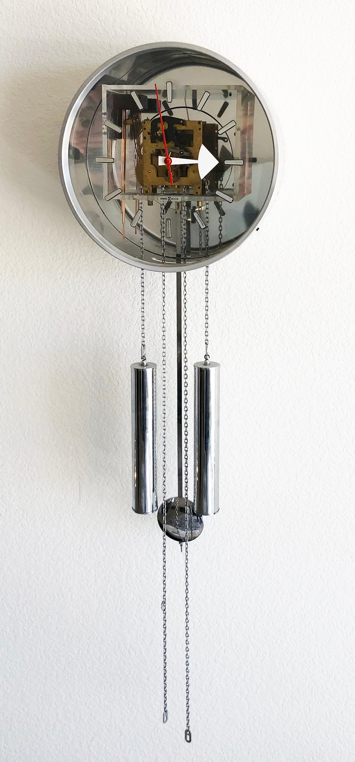 A truly stunning modern wall mounted clock by George Nelson for Howard Miller. This pendulum wall clock features a transparent acrylic face that allows you to see all the inner-working mechanisms. The striking white hour hand and bold red minute