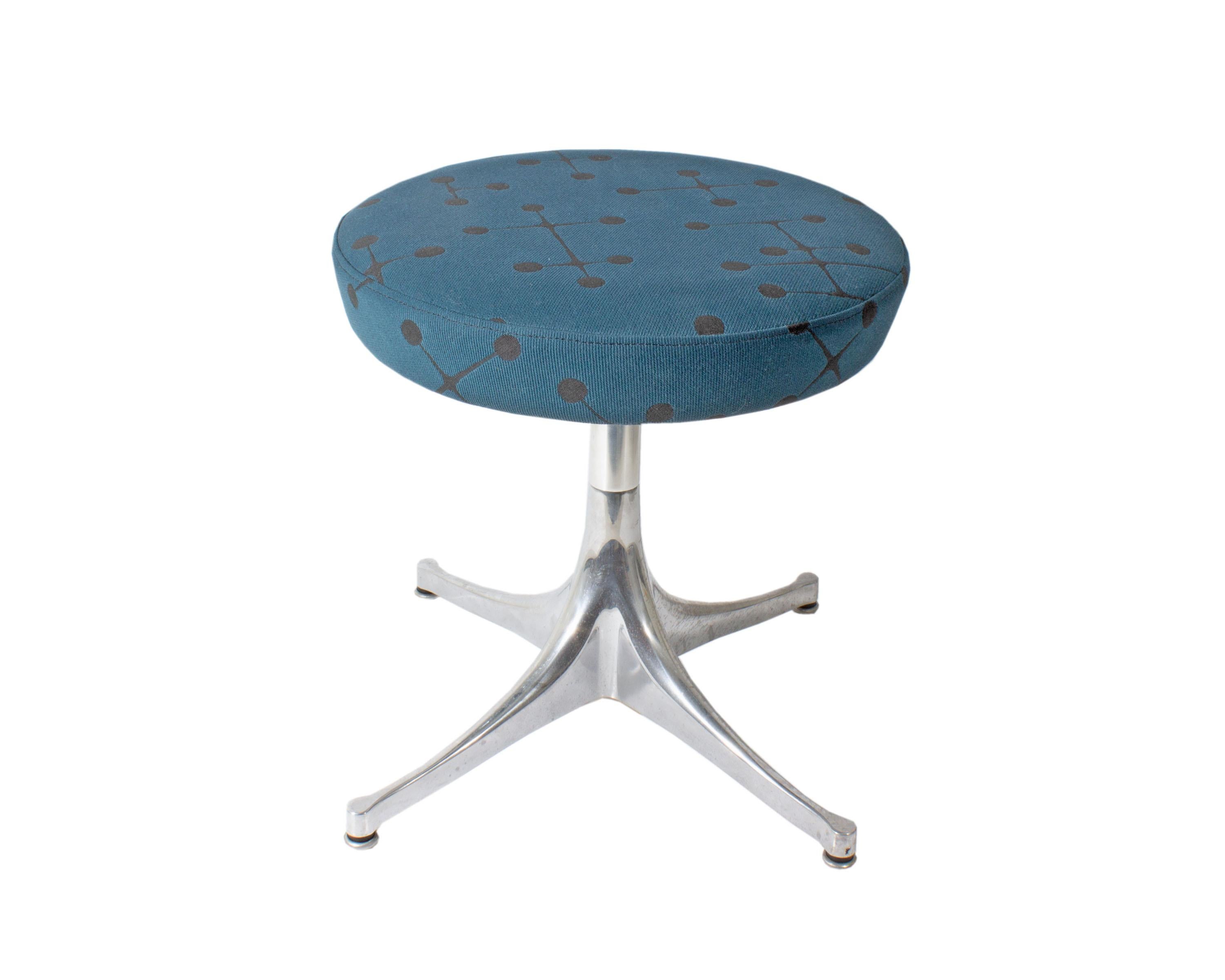 A pedestal stool originally designed by American designer George Nelson (1908-1986) for Herman Miller. The round stool features a padded seat covered in a galactic blue upholstery with a black atomic pattern by Maharam. The stool stands on a metal