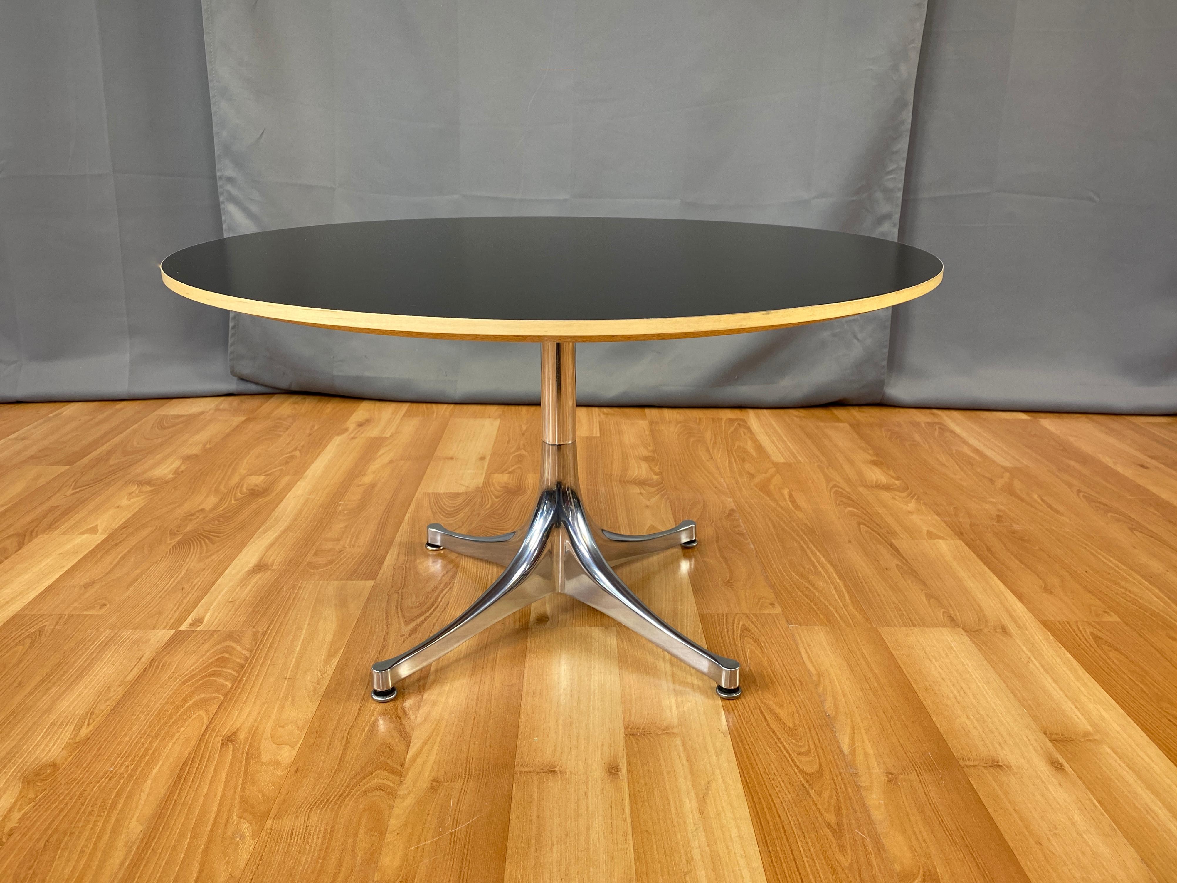 Offered here is a George Nelson design pedestal coffee table for Herman Miller.
Tapered legs rise up to a single polished aluminum column, which holds the large black round laminate top that's bordered in beech.