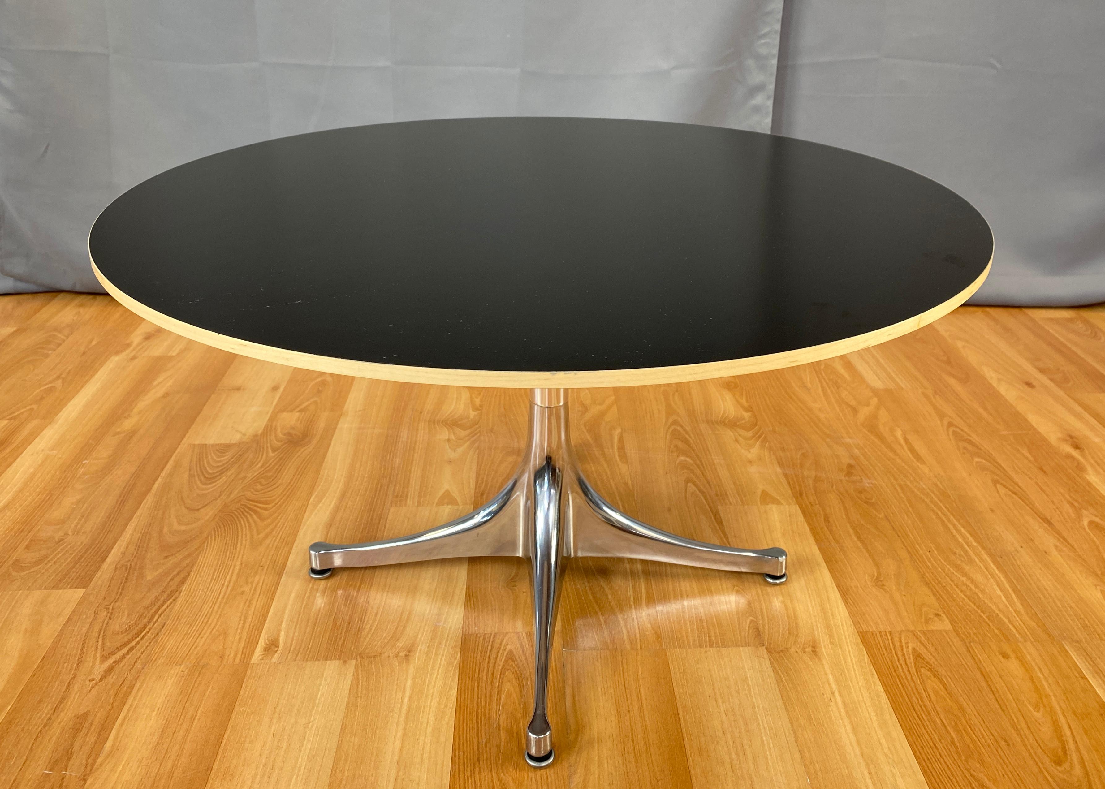 Offered here is a George Nelson design pedestal coffee table for Herman Miller. 
Tapered legs rise up to a single polished aluminum column, which holds the large black round laminate top that's bordered in beech.