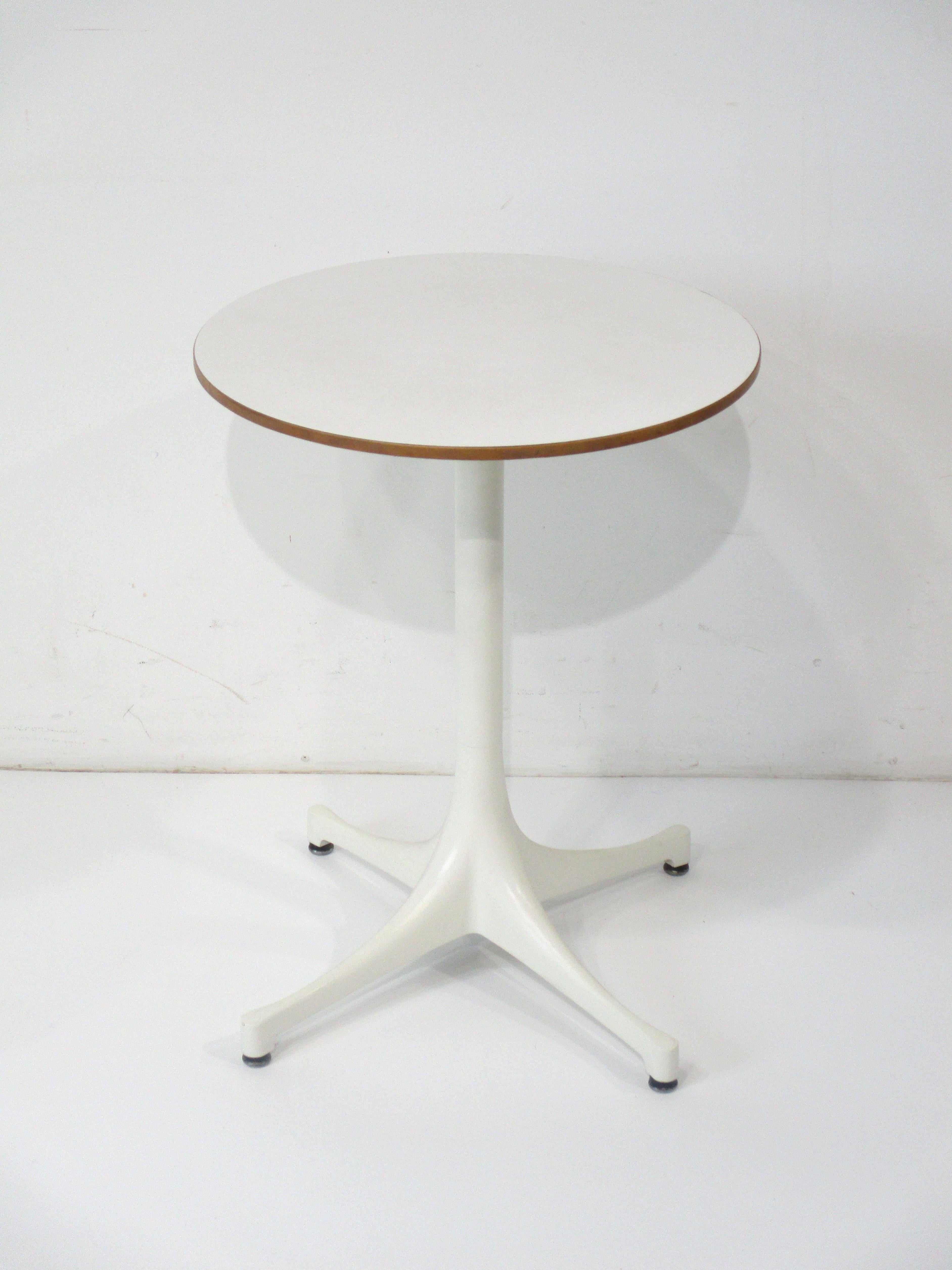 A simple and elegant pedestal side table with round top having a natural thin wood trim detail to the edge and cast meat star base . The base with foot pads to protect your floors has a top in white Lamanite , manufactured by the Herman Miller