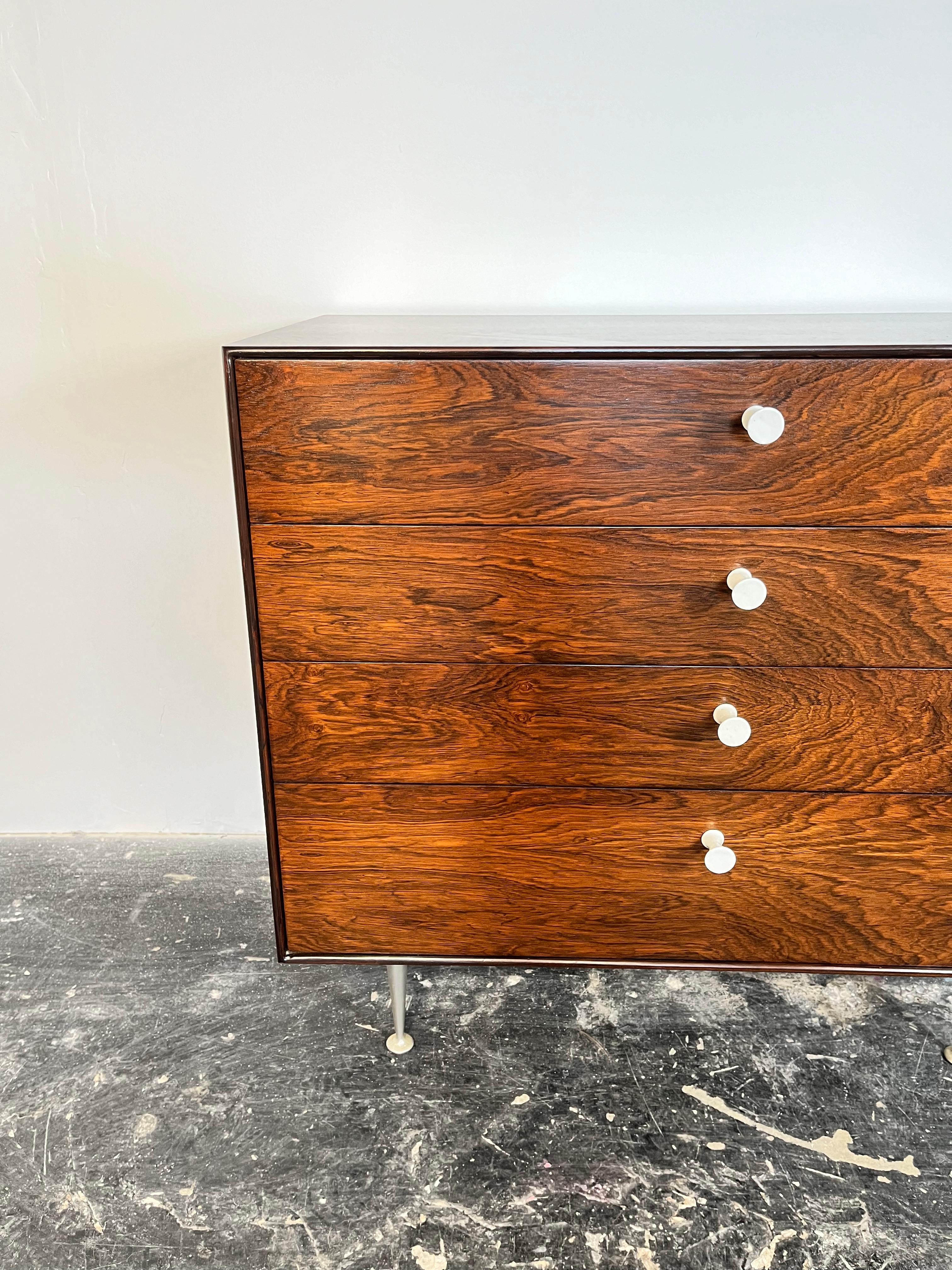 A rosewood thin edge chest designed by George Nelson for Herman Miller with exquisite rosewood grain and early original white porcelain handles. 

The George Nelson Rosewood Thin Edge 4-drawer Dresser, crafted by Herman Miller, epitomizes the