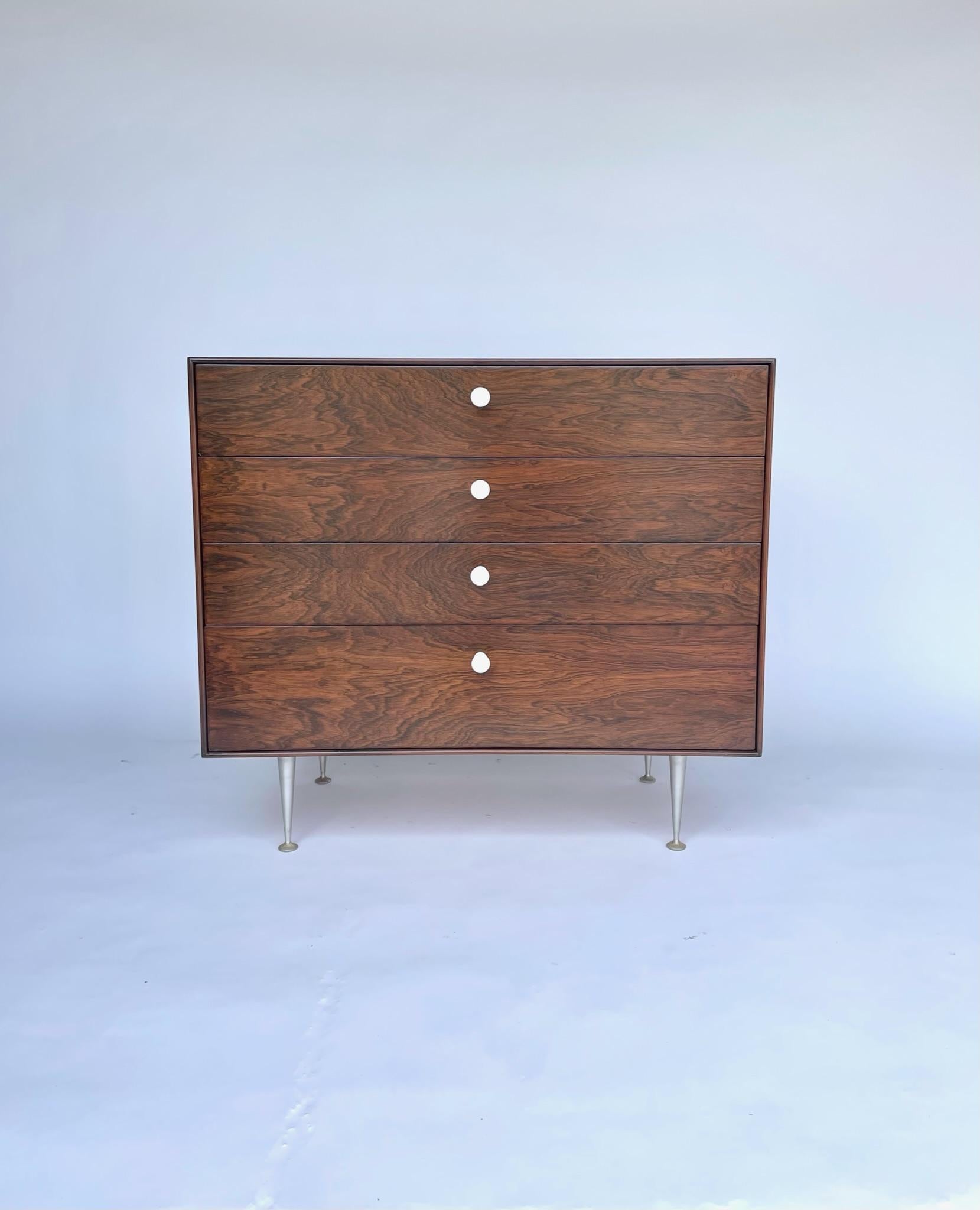 A rosewood thin edge chest designed by George Nelson for Herman Miller with exquisite rosewood grain and early original white porcelain handles. 

The George Nelson Rosewood Thin Edge 4-drawer Dresser, crafted by Herman Miller, epitomizes the