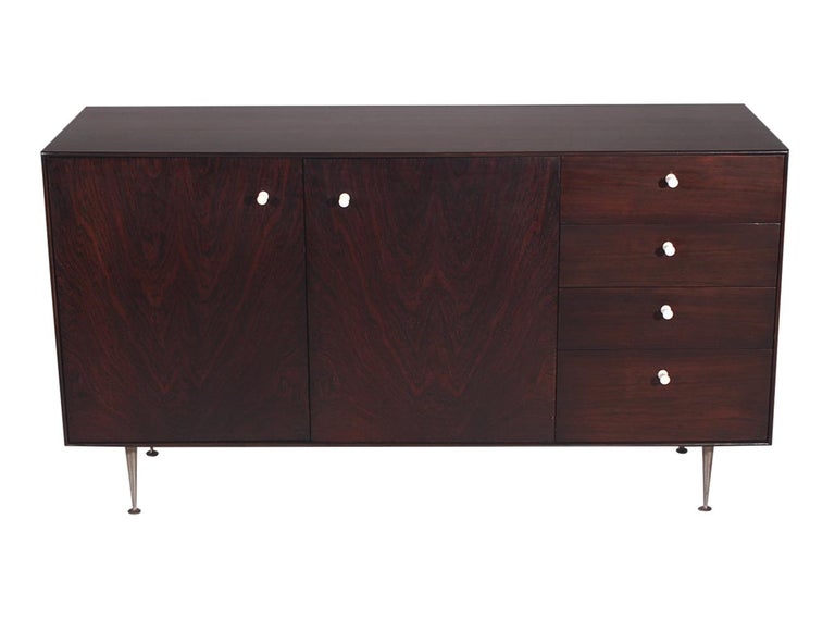 A nice early example of a thin edge cabinet designed by George Nelson and produced by Herman Miller. This piece features beautiful rich dark rosewood, turned aluminum legs, and white lacquered replacement knobs.