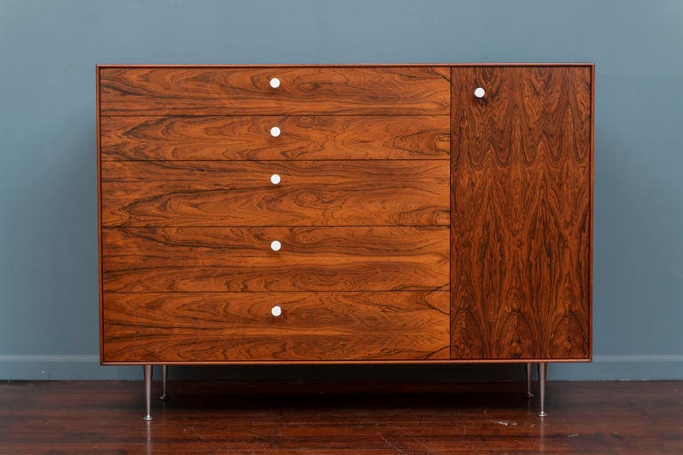 George Nelson design thin edge series tall dresser for Herman Miller, 1958.
Made from exceptional figural rosewood veneer on aluminum tapering legs. Featuring five graduating drawers with fitted dividers in two and a side cabinet with two