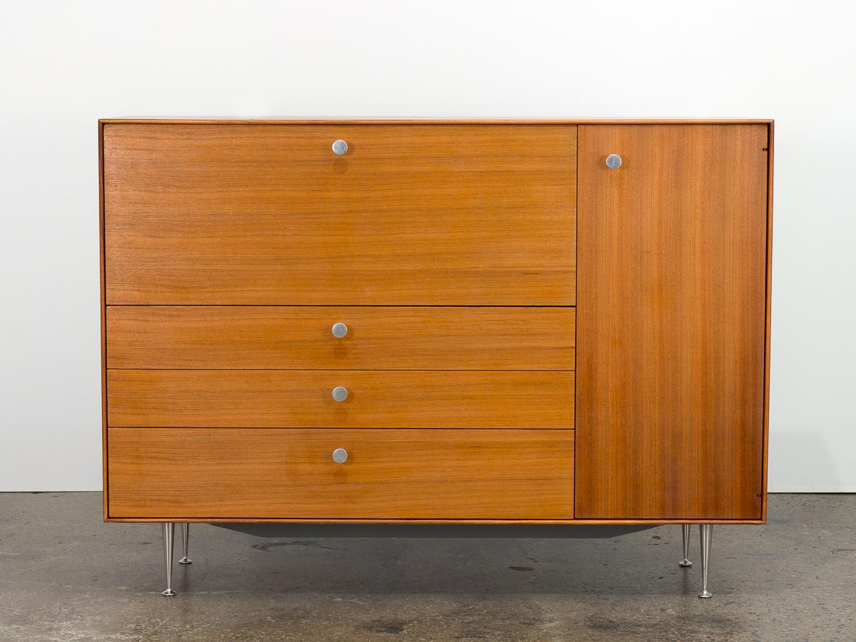Thin edge secretary cabinet designed by George Nelson for Herman Miller. Named for its clean lines, the minimal walnut case floats on aluminum champagne flute legs and finished with Nelson's signature satin knobs. Panel drops down to reveal a