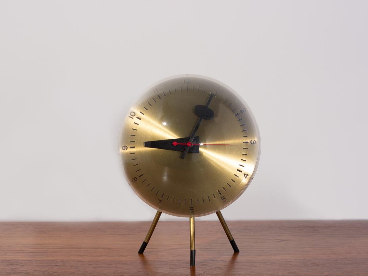 Scarce large tripod table clock, Model 4764, designed by George Nelson and Associates for Howard Miller Clock Company. Satin brass dial encased in plexiglass bubble, with signature bold black hands, red second hand, and modern numerals. Gleaming