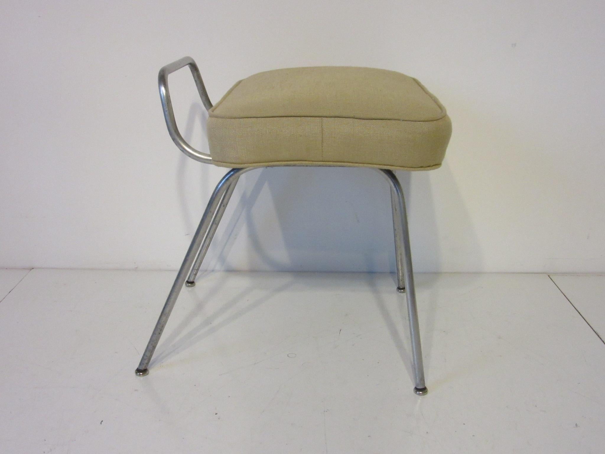 A satin aluminum based vanity stool with upholstered cushion and rubber / metal foot pads designed by George Nelson model #4672 produced in the early 1950's by the Herman Miller Furniture company.