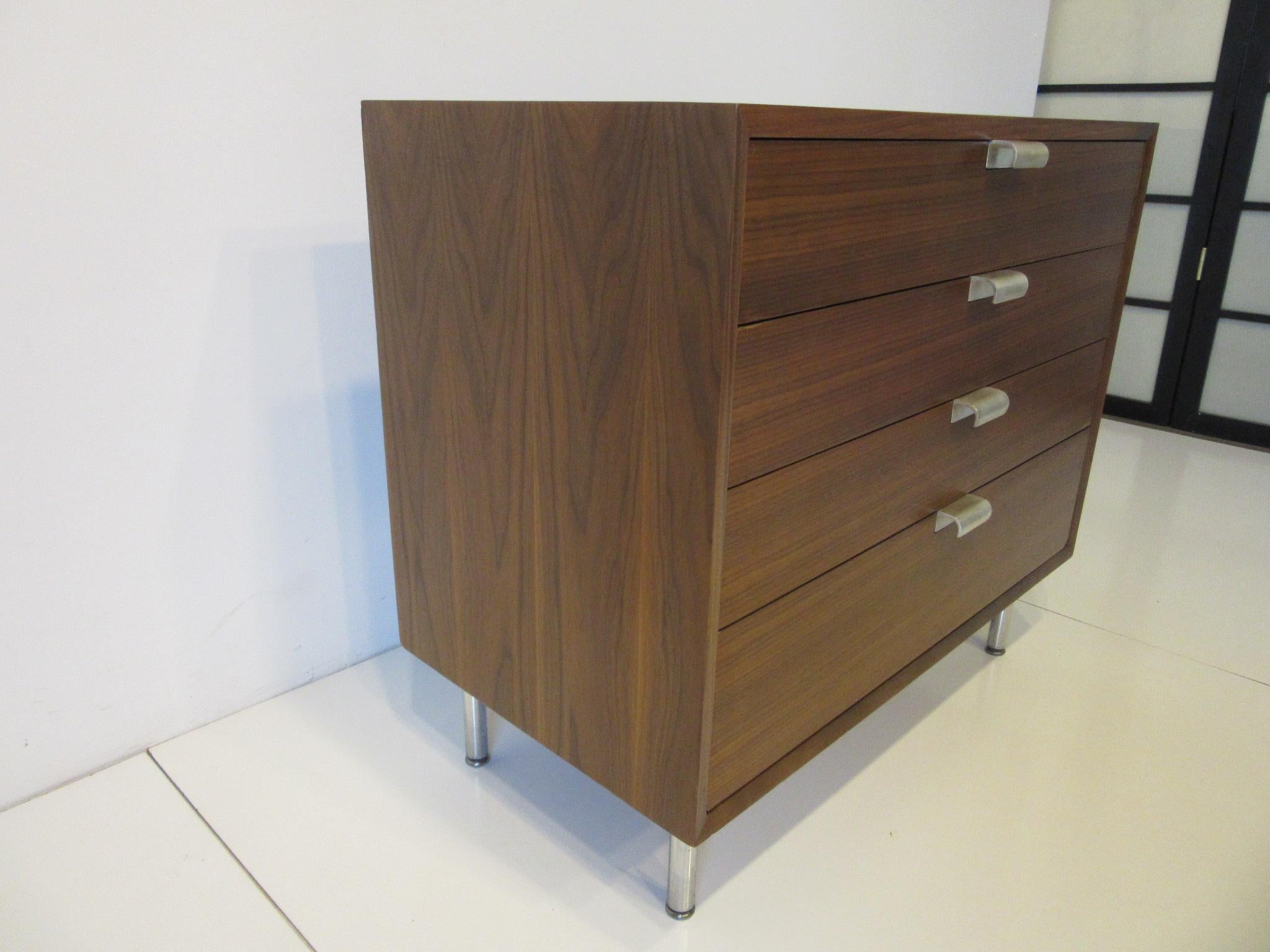 A beautiful medium toned walnut chest / dresser with great gaining to the overall piece making it an eyecatcher, four-drawer with silver large J pulls and chrome tubular legs. Retains the original early foil labels from the Herman Miller Furniture