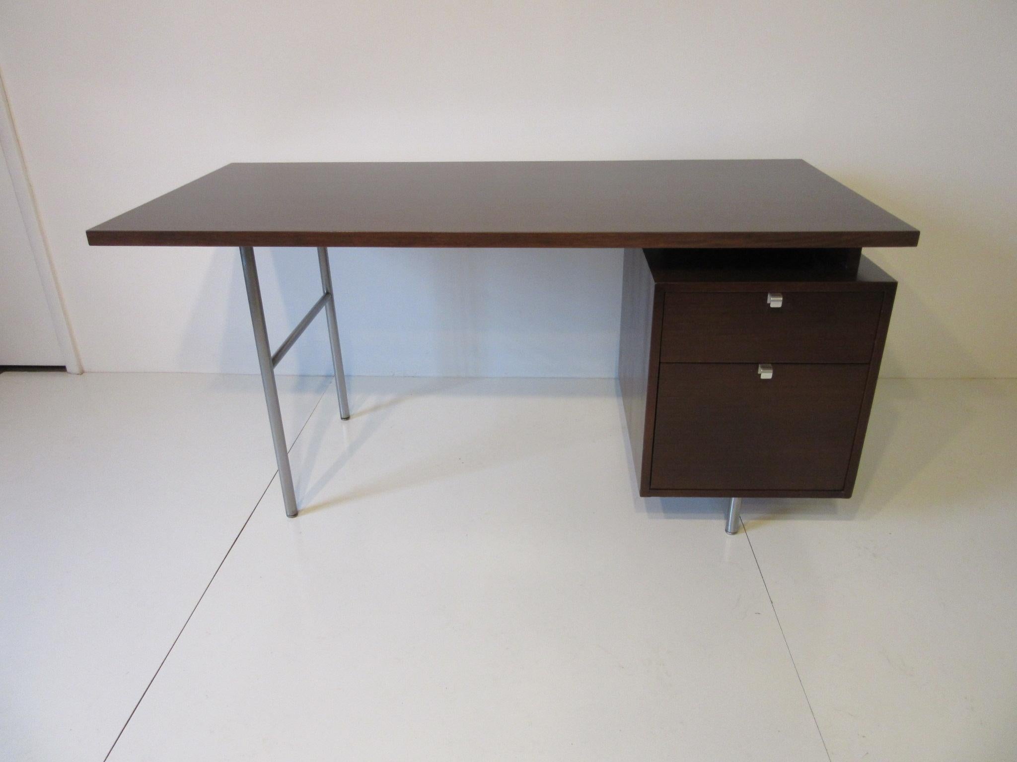 A dark walnut desk with floating top, a smaller drawer and large file drawer to one side with aluminum J pulls sitting on satin chromed legs. Manufactured by the Herman Miller furniture company.