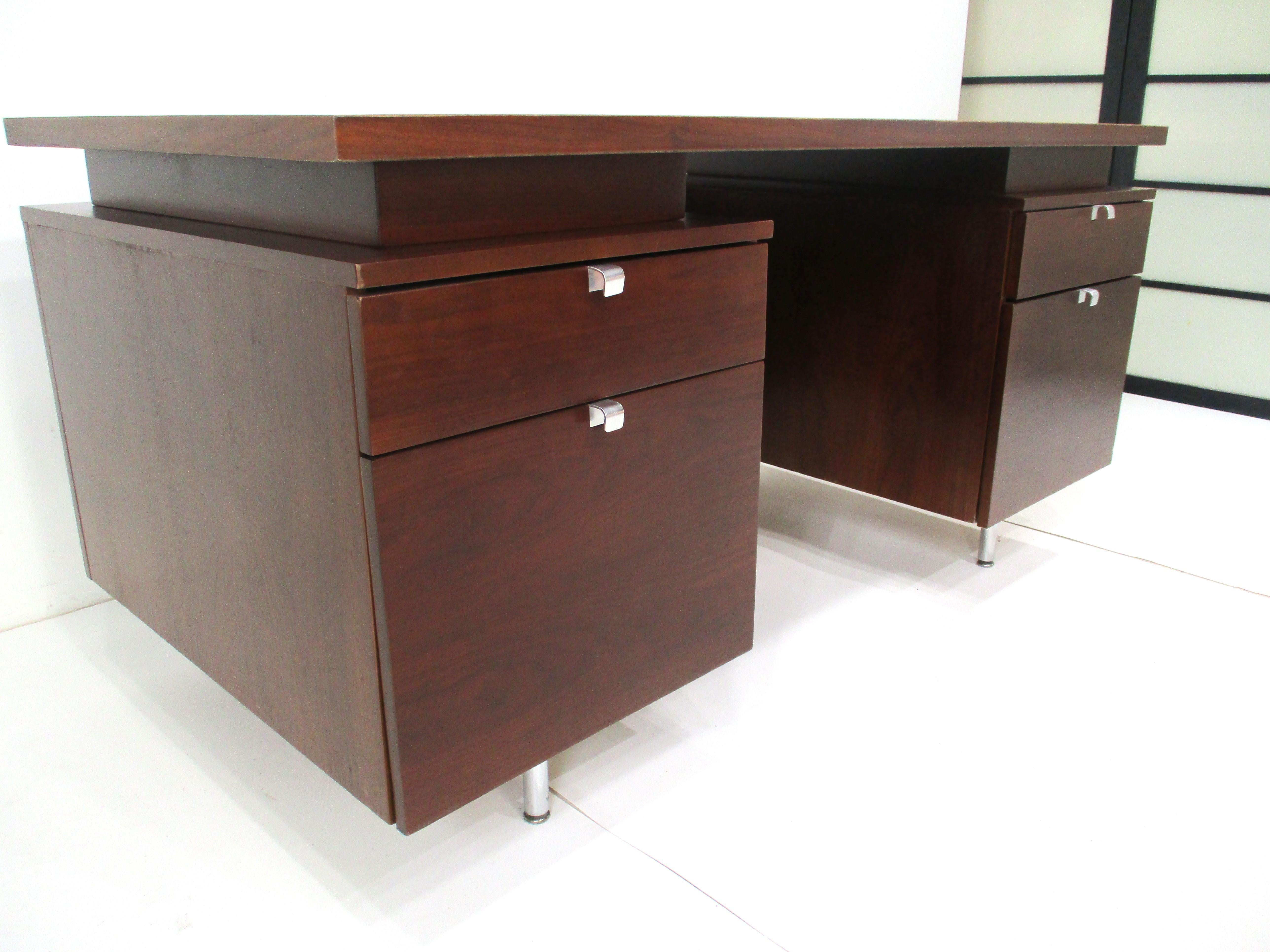 A dark walnut executive desk with a floating top having a smaller drawer and larger file drawer to each side . Aluminum pulls and brushed stainless steel legs enhance the look and feel of this very well crafted piece . The desk comes from the Irwin
