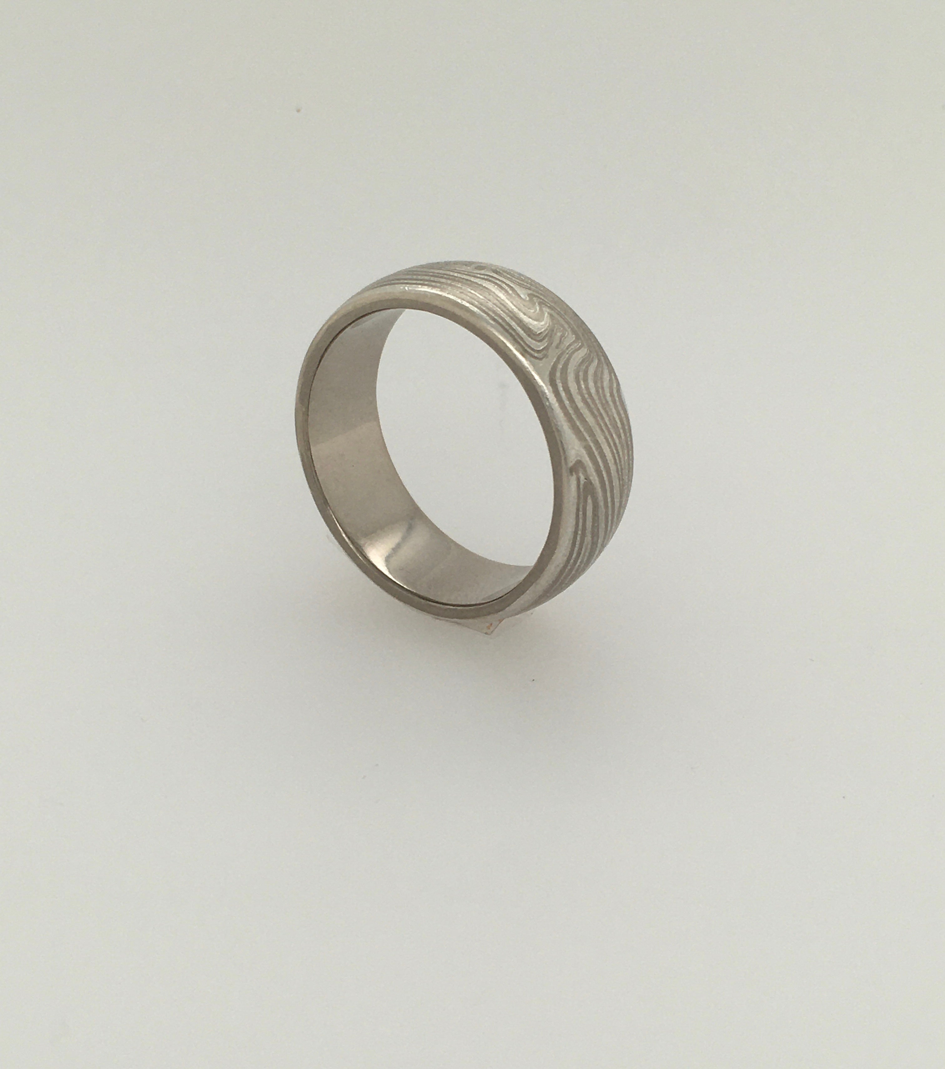 A striking 8 mm half-round wedding band by George Stone in the traditional Mokume style.  The band features 14K gray gold and etched sterling silver.  Interior stamp reads 