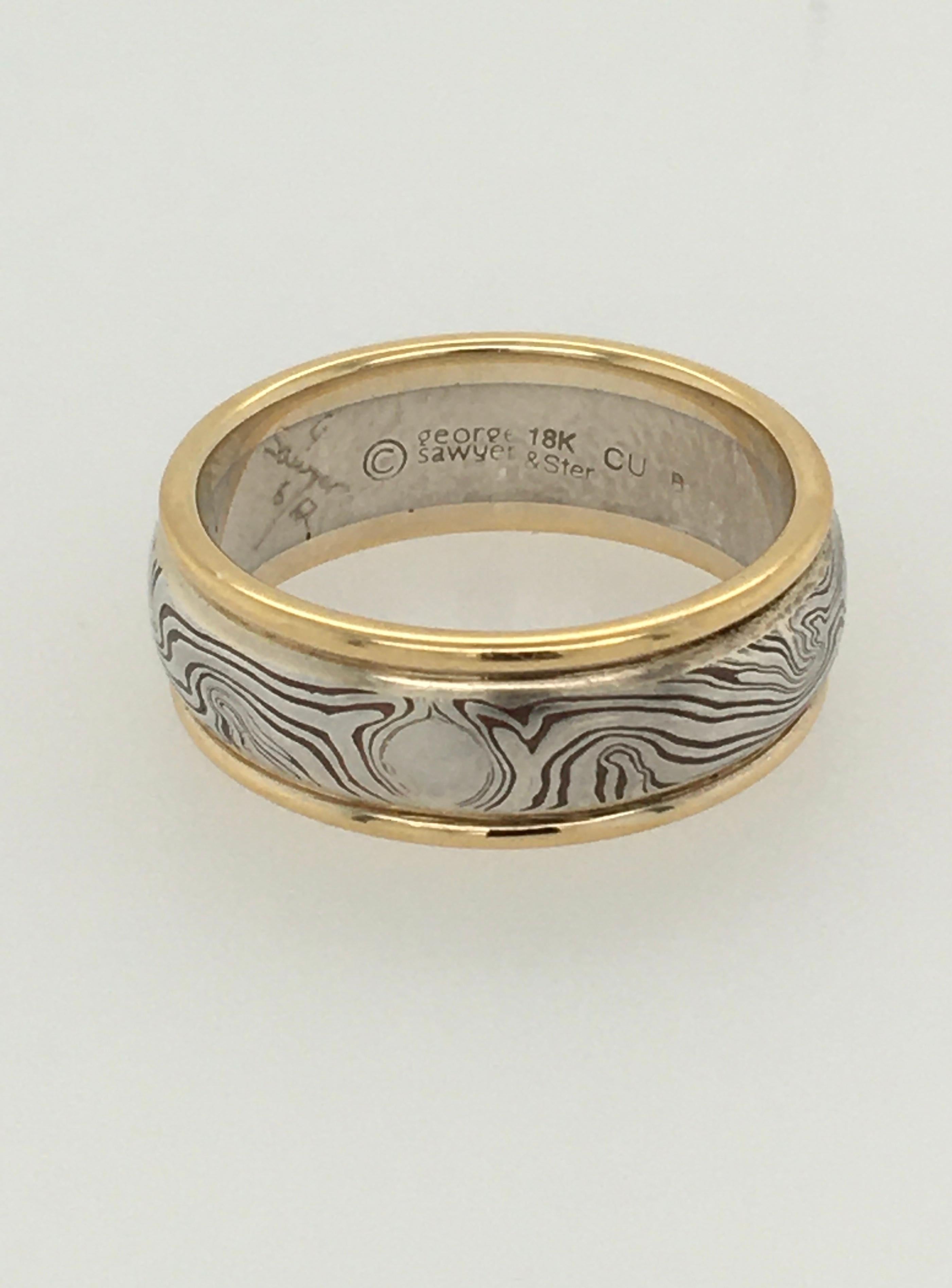 A striking round edge wedding band in the traditional George Sawyer Mokume style.  This 8 mm ring features 18K yellow gold edges surrounding sterling silver & etched copper. Interior stamp 