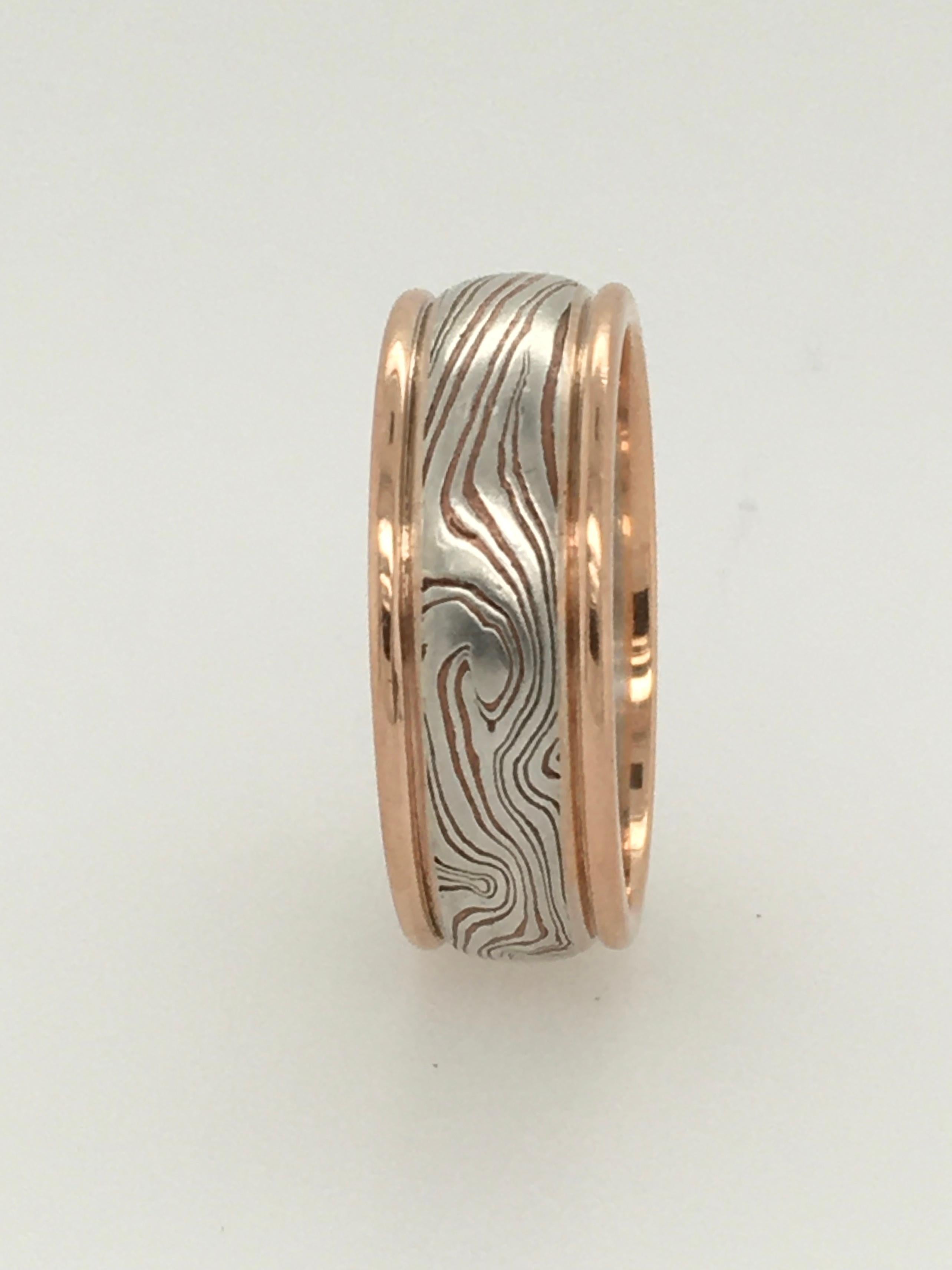 A striking round edge George Sawyer wedding band in the traditional Mokume style.  This 8 mm ring features 14K red gold edges that surround sterling silver & etched copper.   Interior stamp 