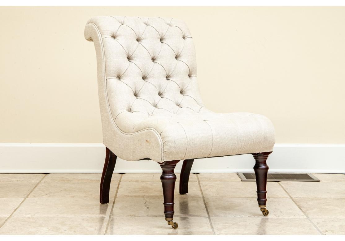 Handmade in England. An elegant slipper chair with sloping rolled back and curved seat. Upholstered in an oatmeal tone fabric tufted overall. Raised on dark stained turned front legs on casters and curved square back legs. 
H. 31 1/2