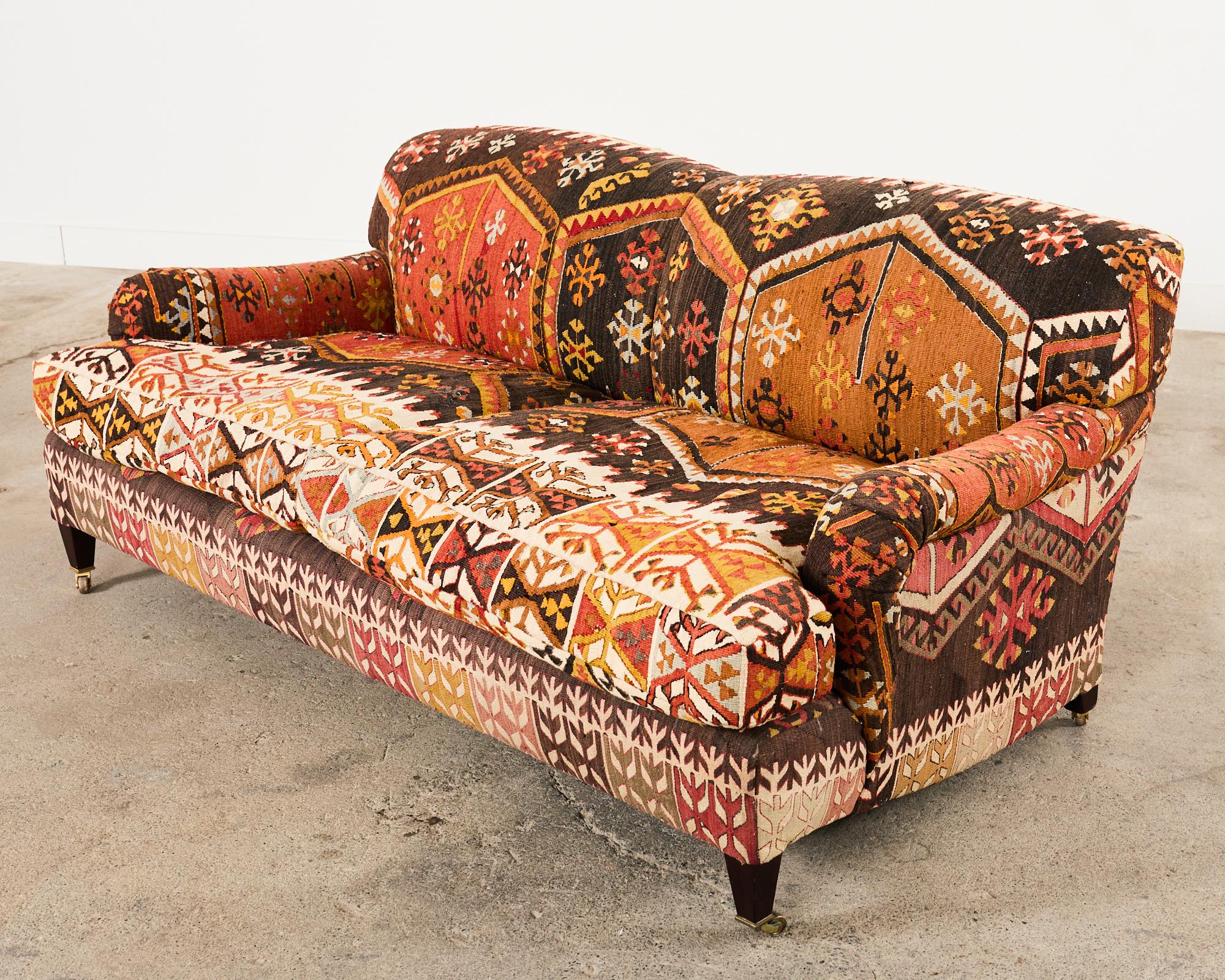 Fantastic English Howard & Sons Style scroll arm sofa created by George Smith artisans. The large signature sofa features a hardwood base upholstered with a dramatic tribal style wool kilim rug. The generous deep seat has fitted cushions filled with