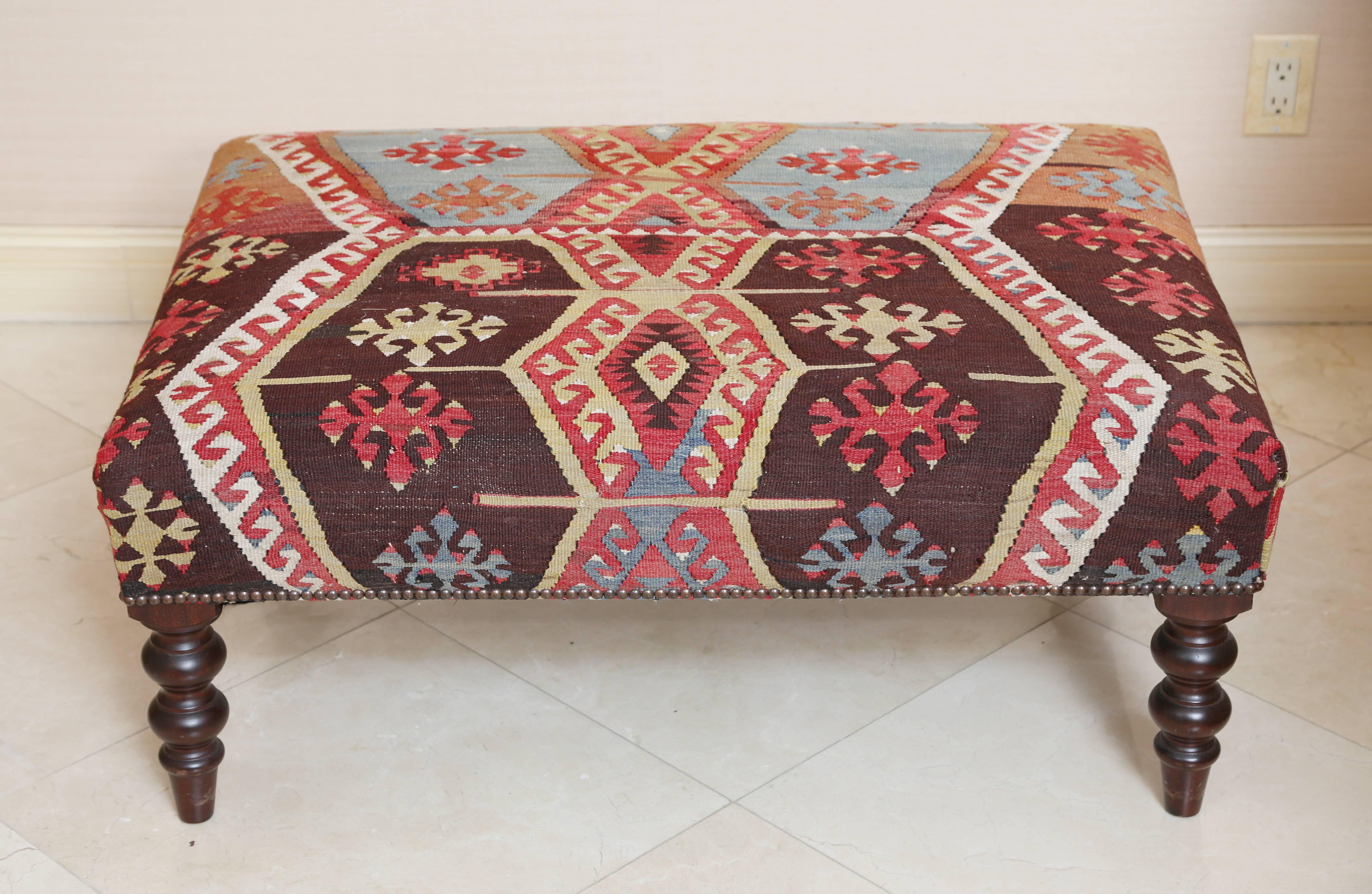 The rectangular seat covered in a Turkish Kilim in browns, reds and sky blue finished with nailhead trim; raised on mahogany ring-turned legs.