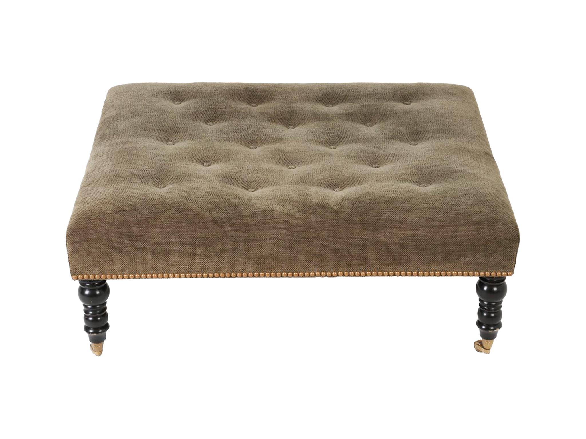This George Smith style ottoman is Edwardian in design, with clean, simple lines and minimal decorative flourishes. The upholstery is an olive-gray velvet weave punctuated with elegant button tufting. Brass studs outline the bottom perimeter, while