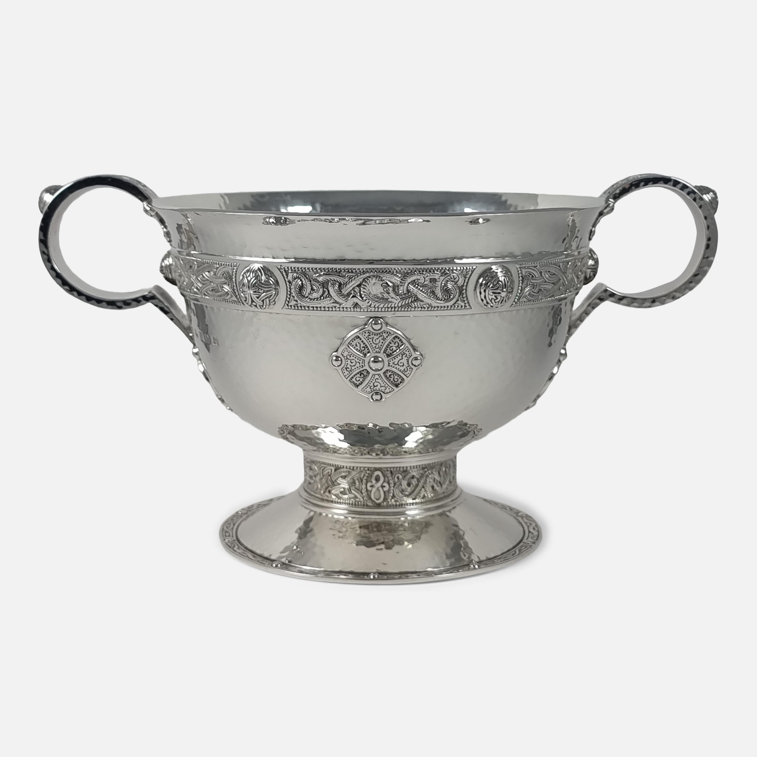 A George V sterling silver Celtic Revival bowl, Glasgow, 1915.

The spot-hammered circular bowl is crafted with an upper band of Celtic knotwork, dragons, bosses and similarly decorated twin hoop handles, on a short column to domed foot, sitting on