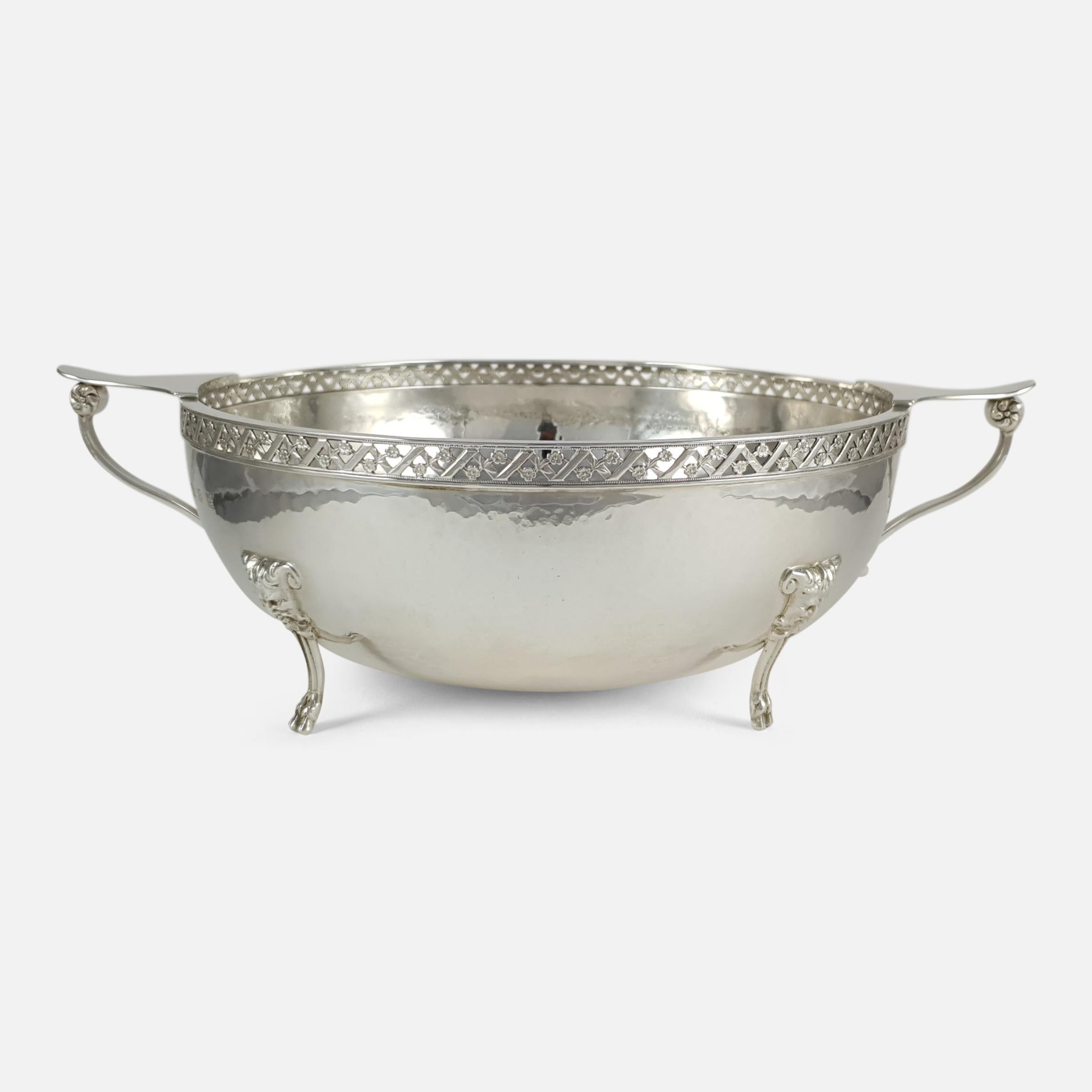 A George V sterling silver Arts & Crafts style bowl with London hallmarks, and by W. Bruford and Sons. The twin-handled bowl is of circular form, spot-hammered decoration, pierced border, scroll side handles, and sitting on four satyr mask mounted