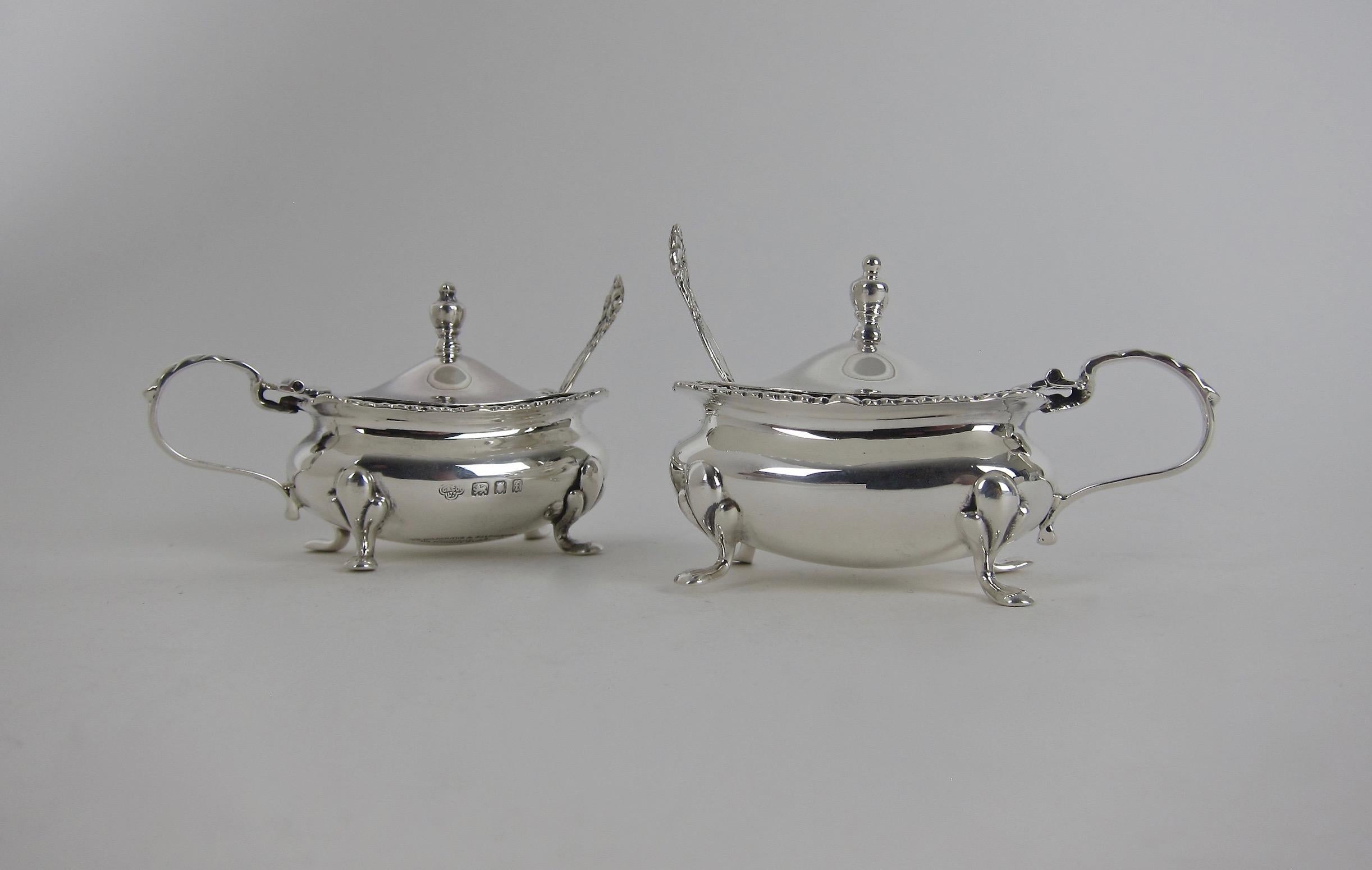 An antique pair of English sterling silver mustard pots with spoons, hallmarked for London in 1921 and 1922 with maker's marks for The Goldsmiths & Silversmiths Co. Ltd. at 112 Regent Street in London.

The unembellished oval bodies were decorated