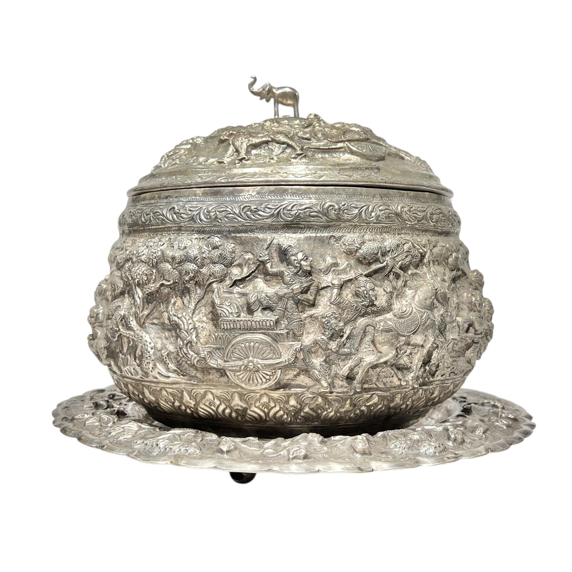 Ciotola da centrotavola in argento birmano di grandi dimensioni con coperchio e sottopiatto con piedini che misura 9 3/4 pollici di altezza e 11 3/4 pollici di larghezza, con eccezionali disegni in repousse e cesellatura con finale a elefante e