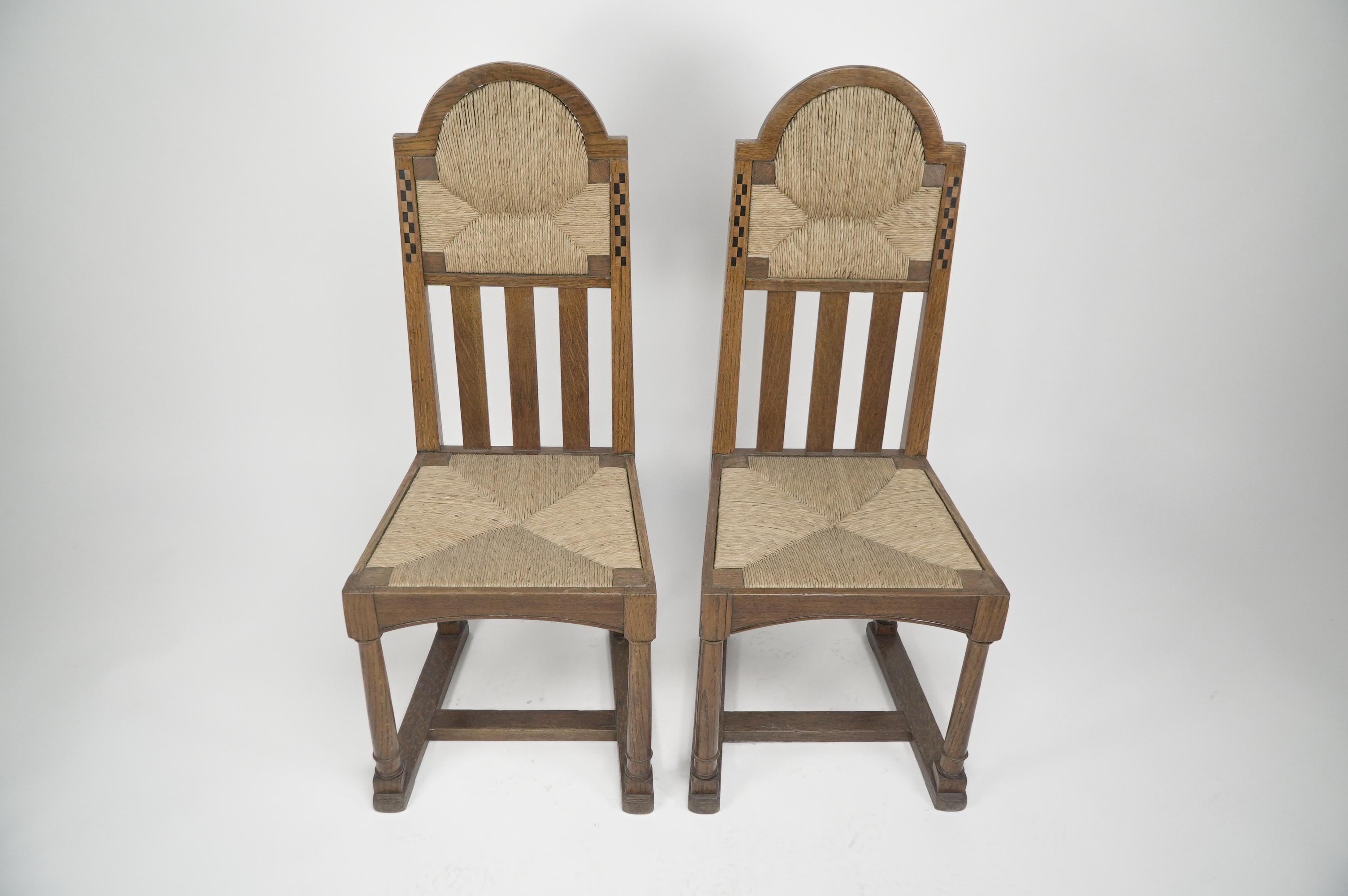 Attribuita a George Walton, una coppia di sedie in quercia in stile Arts and Crafts Glasgow con vistosi intarsi in ebano e bosso, sedile e poggiatesta in giunco con gambe tornite e barelle ad H. 

 