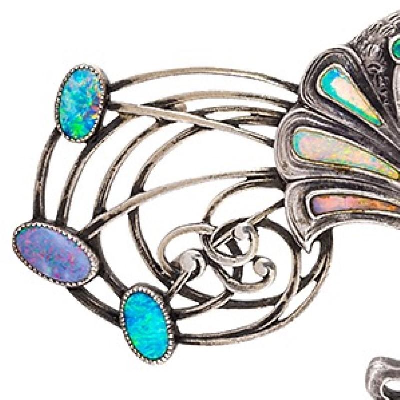 A French Art Nouveau silver cloak clasp with opals by Georges Fouquet. The cape clasp is decorated with 14 bezel set crystal opal plaques.  The clasp is designed as two intertwined peacocks with extravagant whiplash 'feathers'. Circa 1900.

Inspired