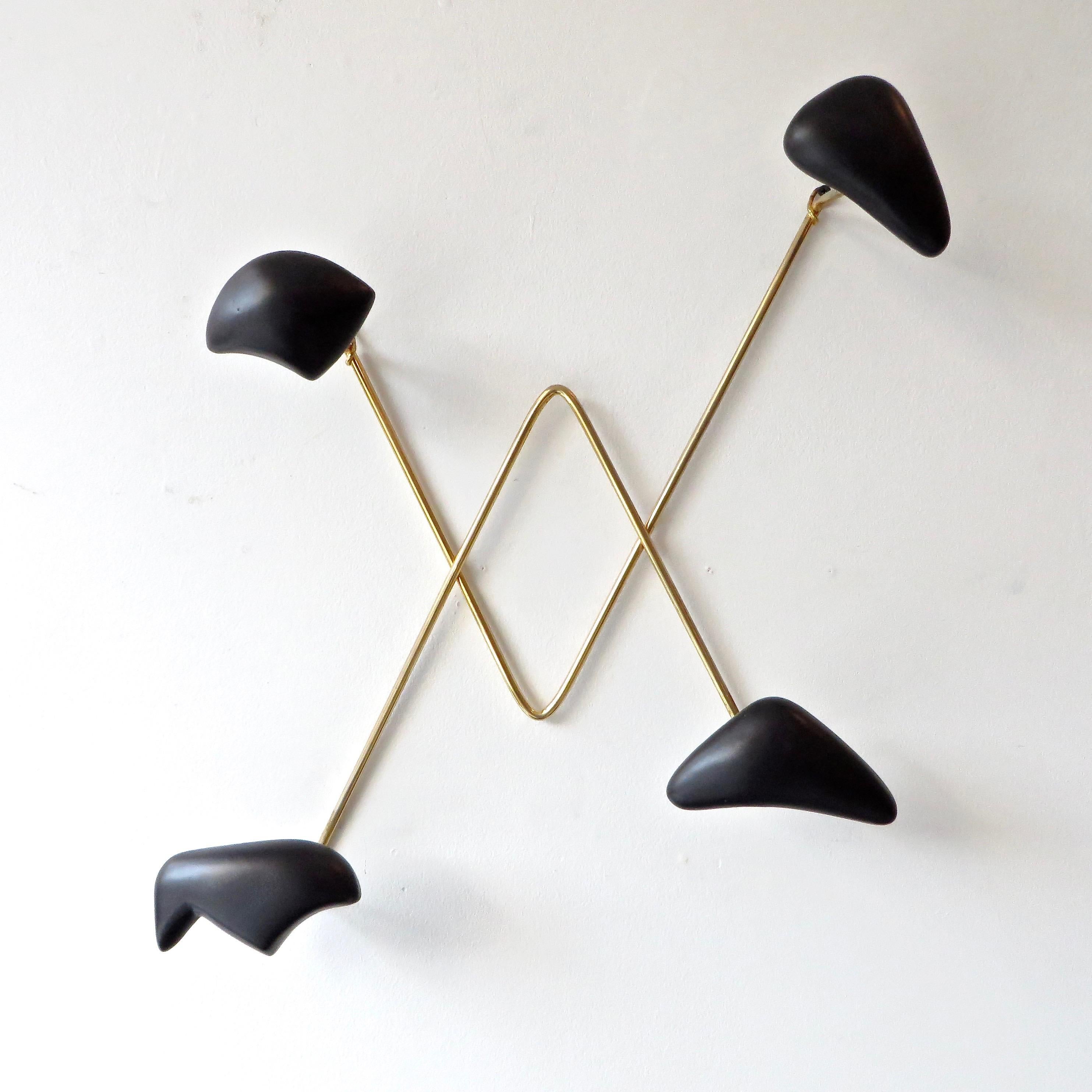 Wall-mounted coat or hat rack by Georges Jouve, produced by Marcel Asselbur, France, circa 1950. Black matte glazed ceramic with brass frame. 
Excellent condition with no chips or restorations. 
