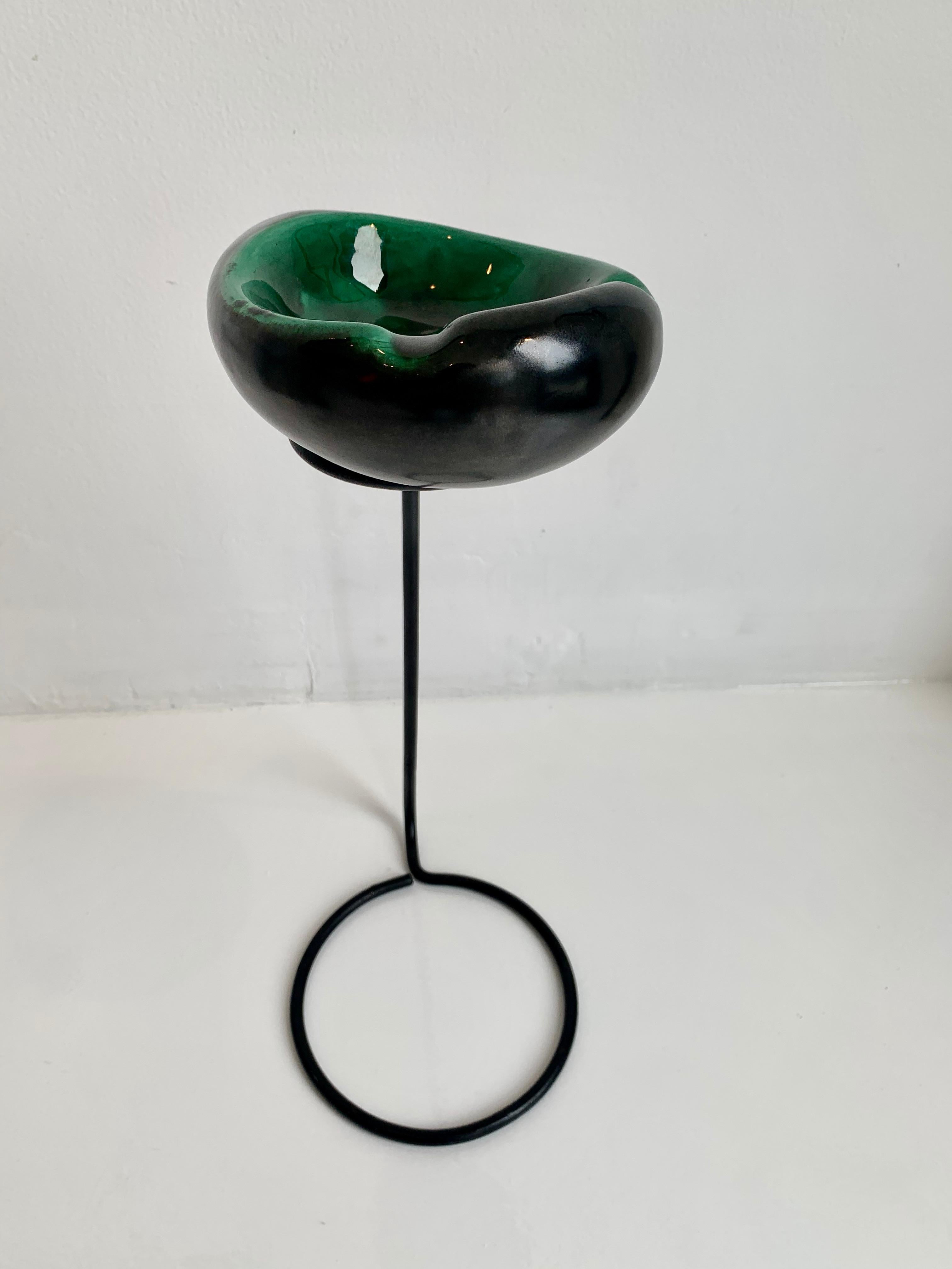Sculptural ashtray/catchall in the style of Matégot and Georges Jouve. Iron frame with circular base and circular top. Green and black ceramic dish sits inside the metal opening. Great lines and coloring. Good vintage condition.