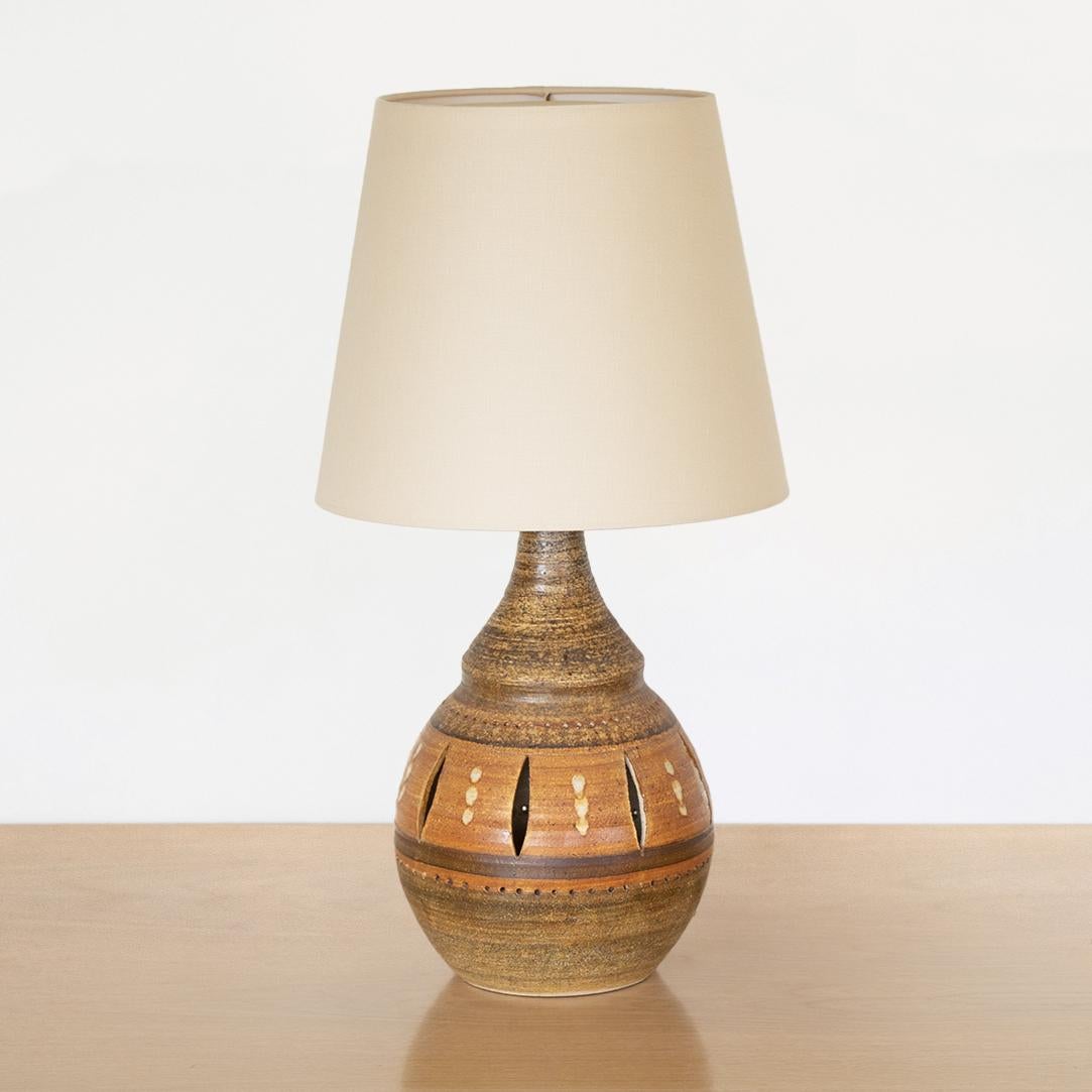 Large French ceramic table lamp from France, 1970's by Georges Pelletier. Round ceramic base in dark beige and brown tones with cut-outs around side. New linen shade and newly re-wired. 


