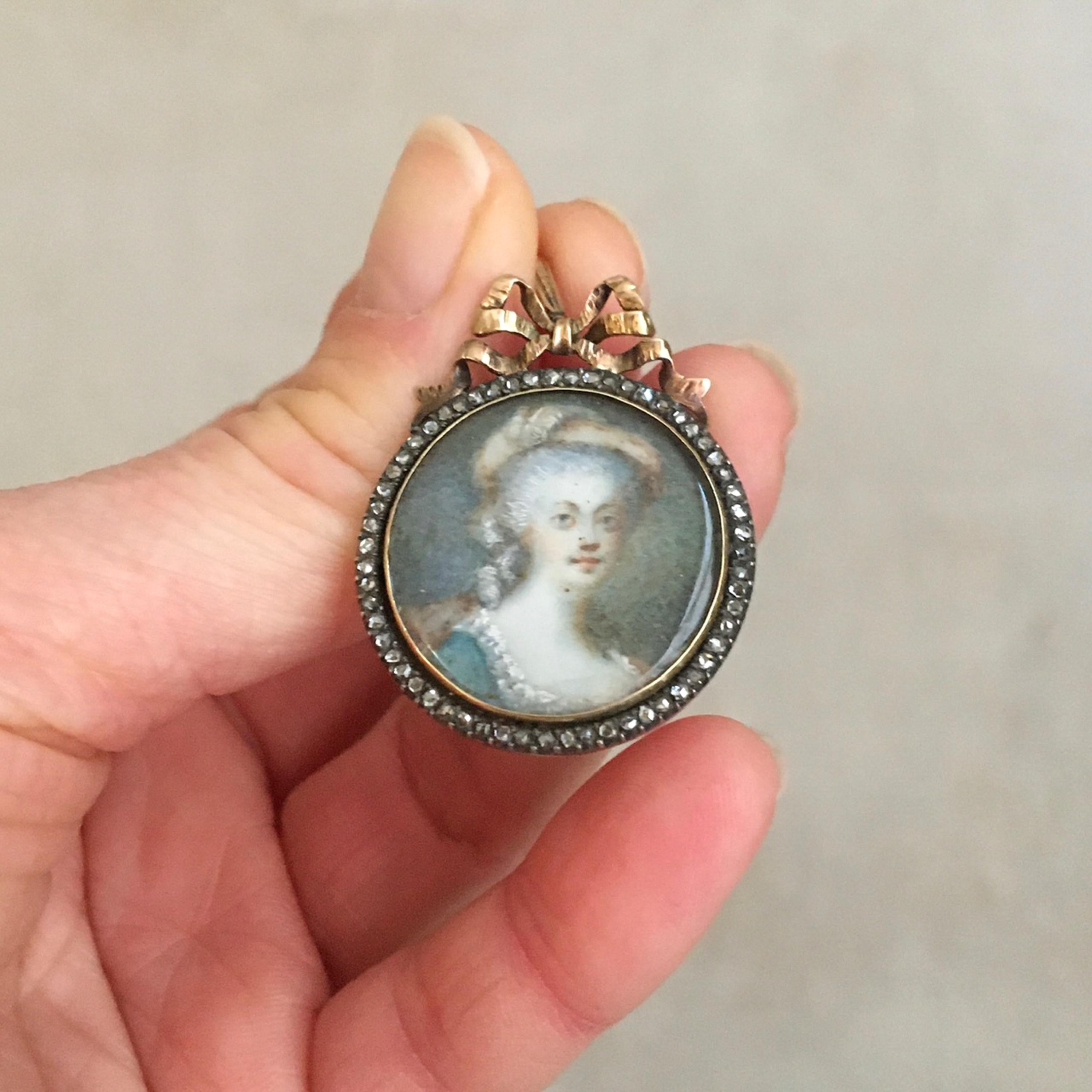 A beautiful antique Georgian (1714 to ca. 1830-1837) 14 karat gold miniature portrait pendant depicting a lady. This portrait, handmade in circa 1800, is painted in soft tones on presumably porcelain and the border is set with 59 rose cut diamonds