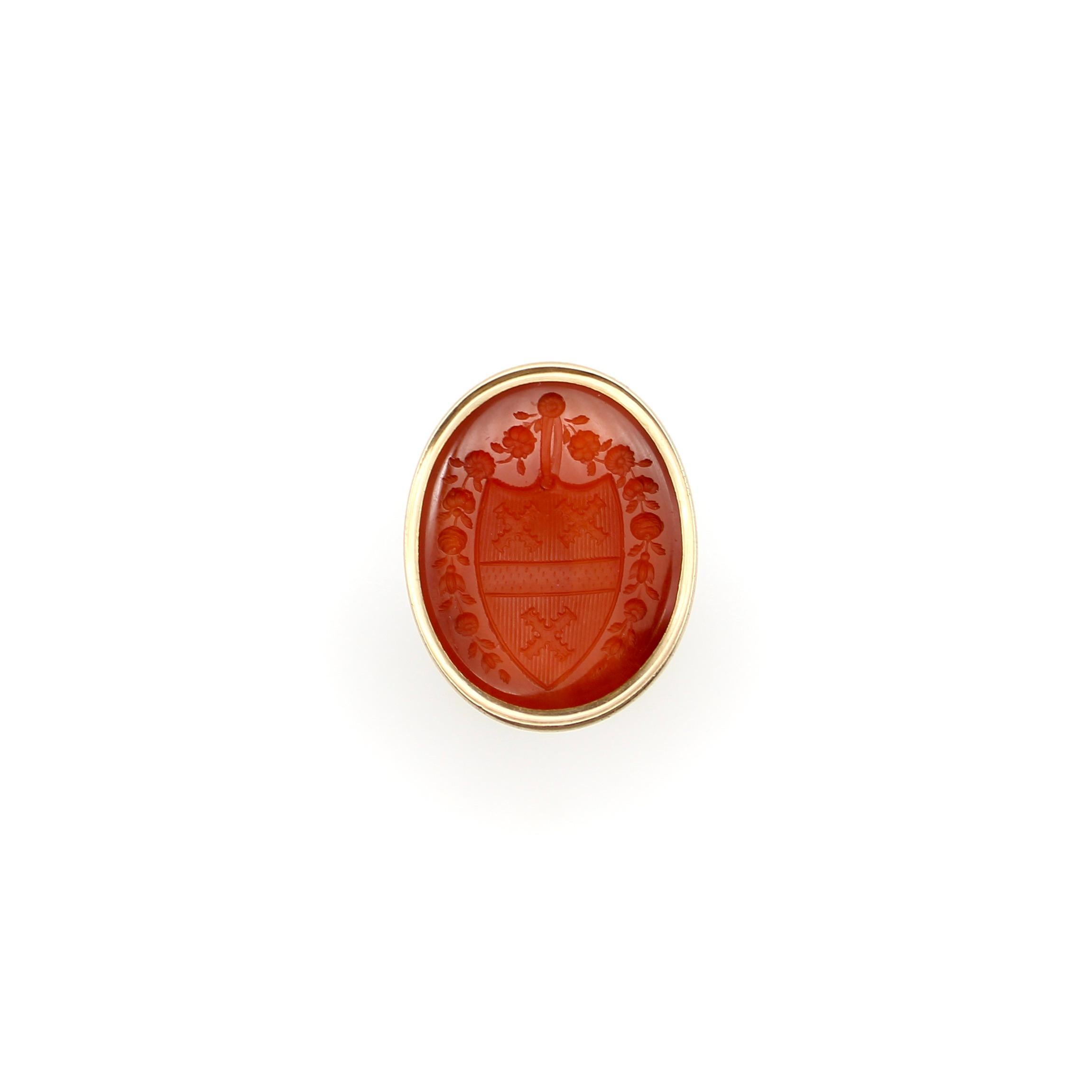 This Georgian intaglio fob features a detailed family crest, carved into beautiful carnelian. The crest contains three crosses, bisected by a dotted bar. Surrounding the crest, a garland of blooming flowers is draped along each side. The intaglio is