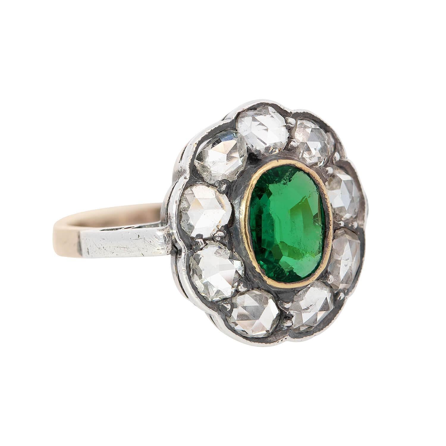 A breathtaking emerald and diamond ring from the Georgian (ca1750s)! Crafted in 14k gold and sterling silver, this stunning ring features an exquisite approximately 0.75ct oval step cut emerald, which is held within a bezel setting. The central