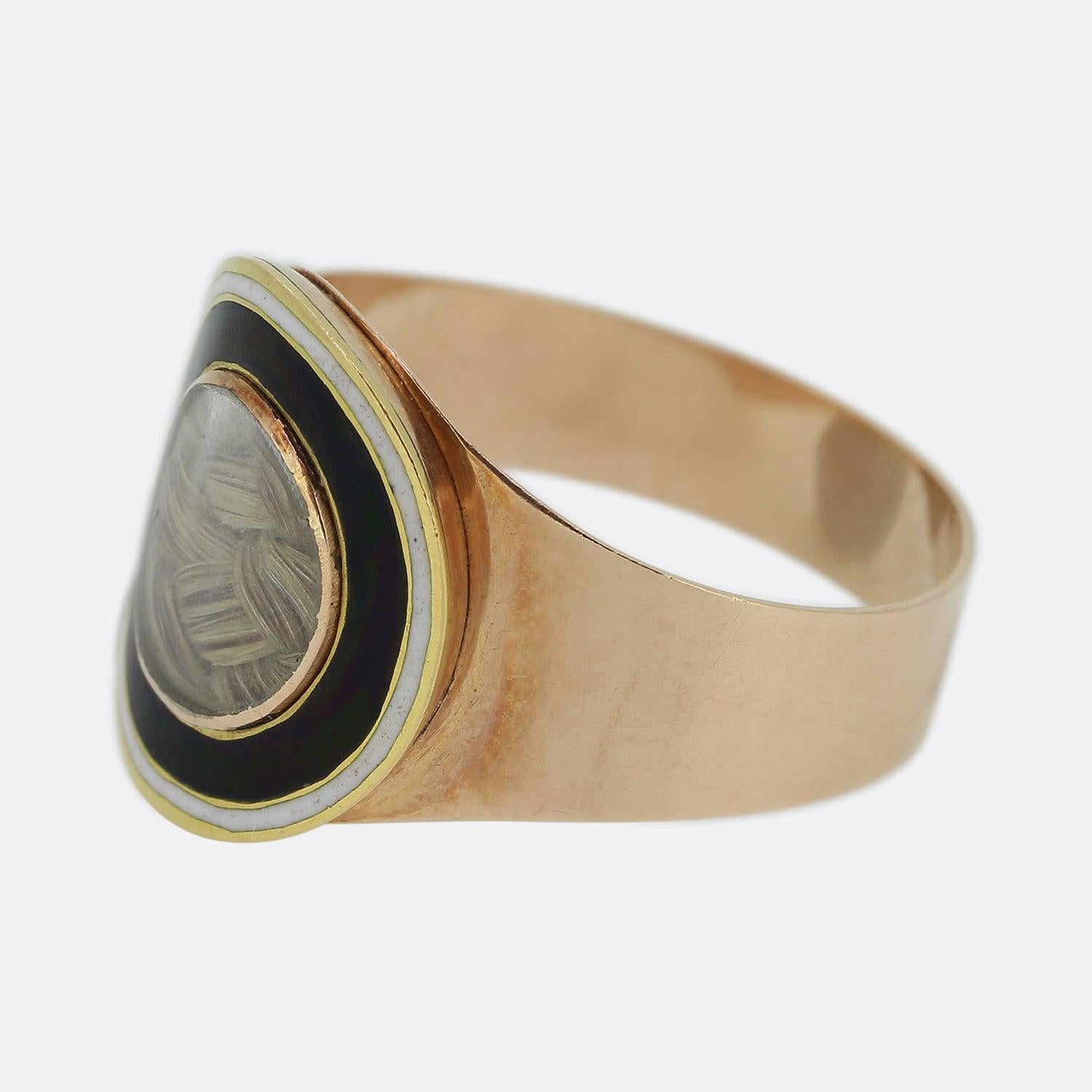 This is a wonderful 15ct rose gold mourning ring from the late Georgian era. The piece has been set with a centralised round window that features a small locket of hair and a border of black and white enamel around the outer edge. The piece is
