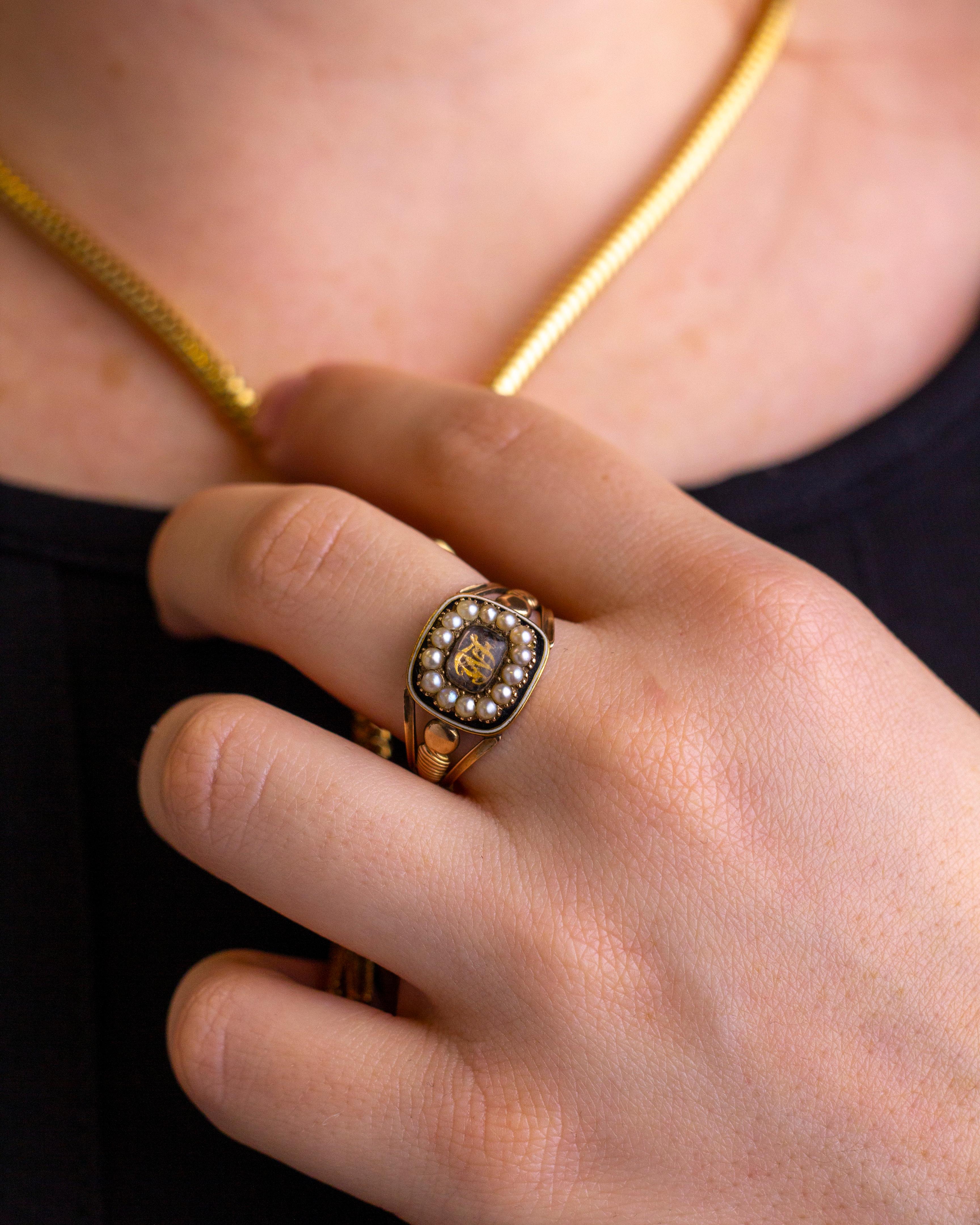 An 18kt yellow gold, black enamel, and seed pearl mourning ring dating to 1817. The piece centres on a piece of likely Essex crystal which sits atop of the letters 'WF' cut from gold. Surrounding this crystal is halo of seed pearls set in a bed of