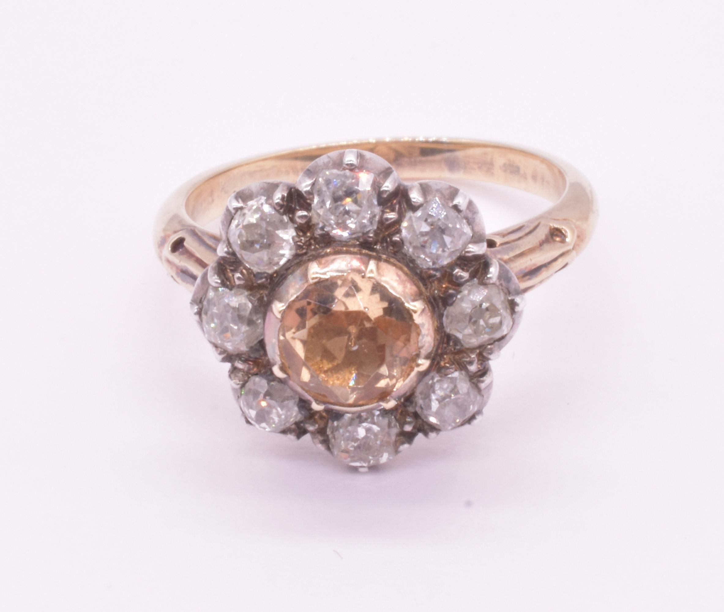 Substantial 18K C1840 diamond cluster ring with 8 round diamonds in a crimped collet setting surrounding a central natural gem, sherry brown topaz and hand set with a decorative band with carved flourishes along the shoulders. The gem topaz was