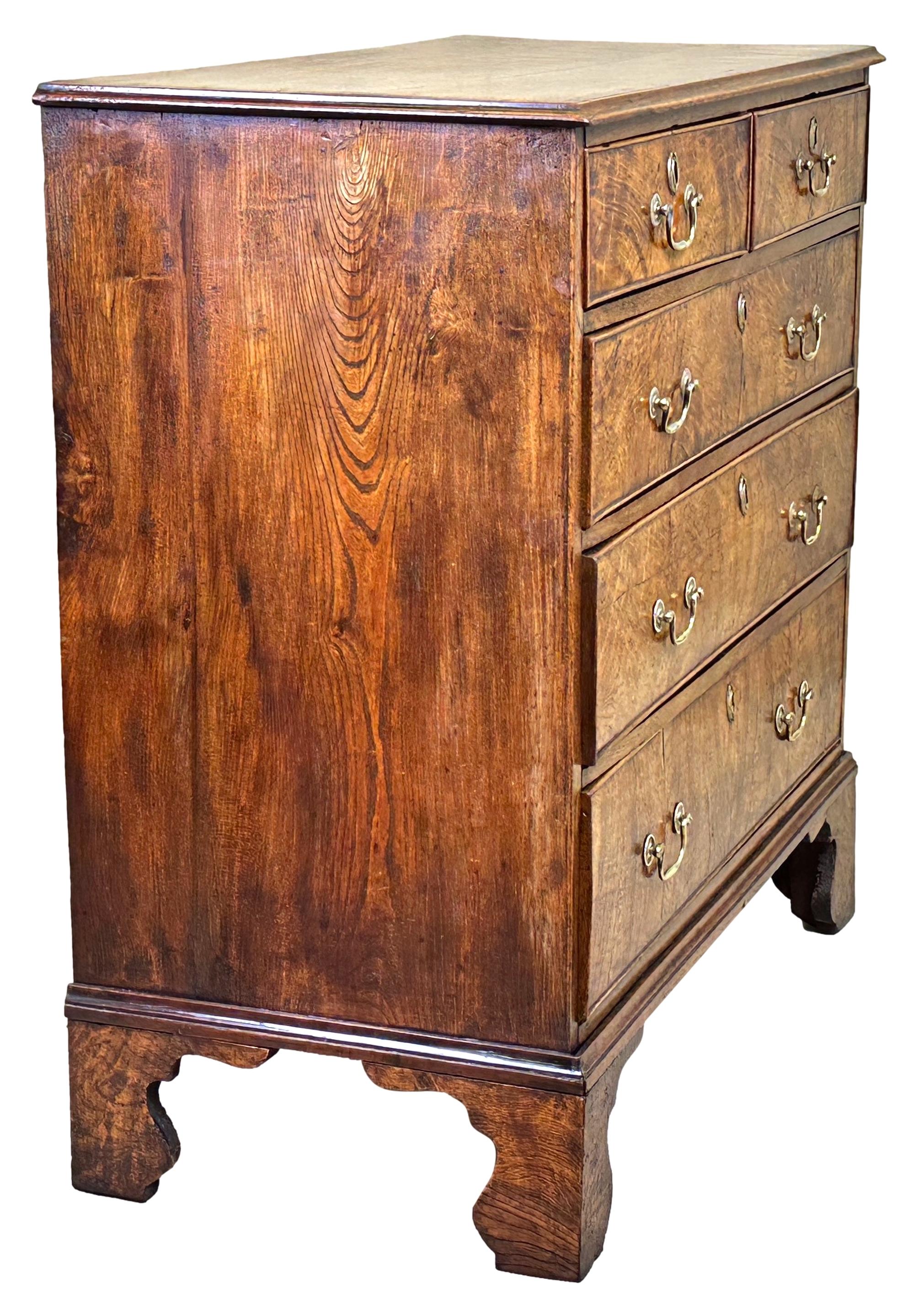 A Delightful Mid 18th Century, George II Period, Elm Chest Having Superbly Figured Top With Attractive Crossbanded Decoration, Over Two Short And Three Long Drawers Retaining Original Brass Swan Neck Handles, Raised On Attractive Original Shaped