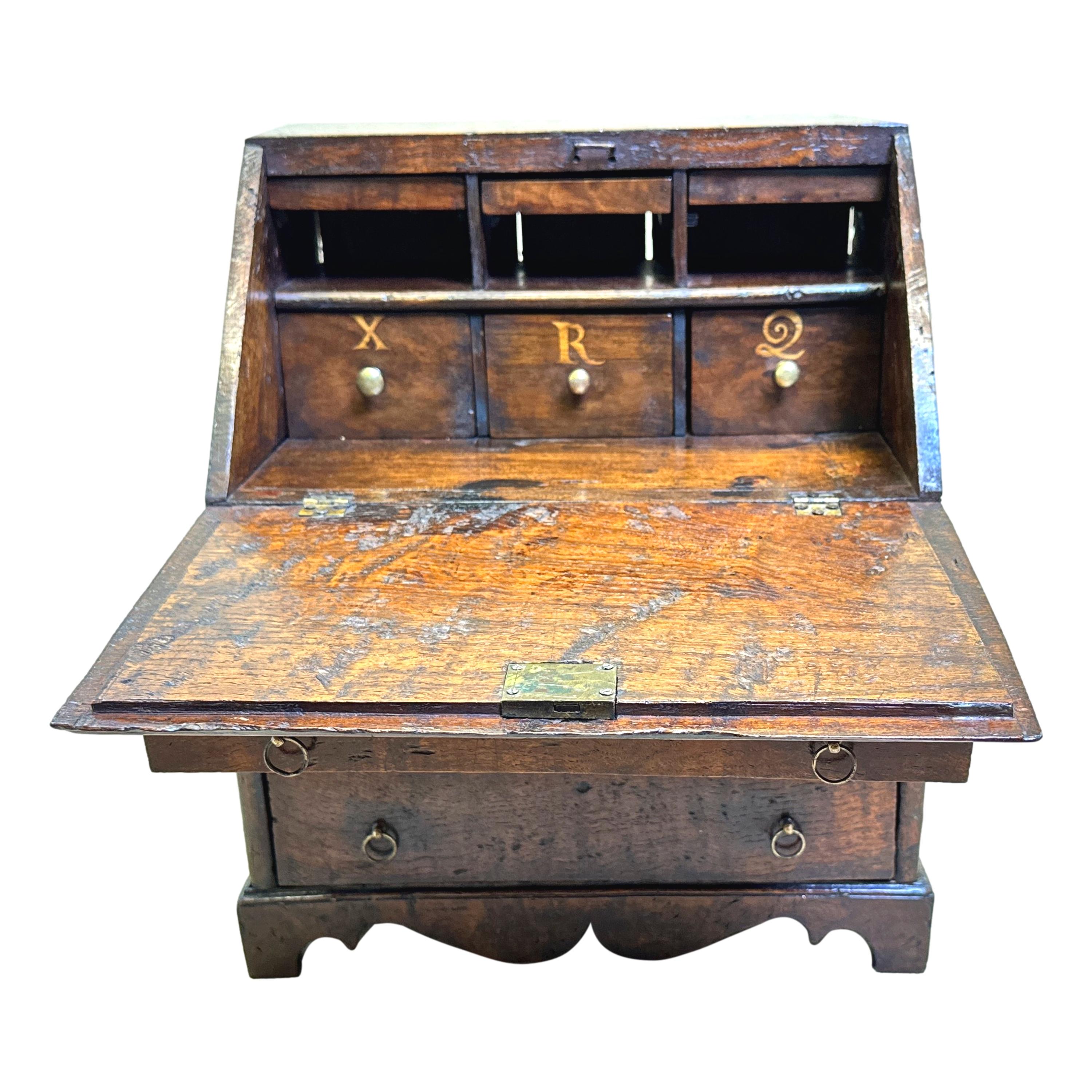 An Extremely Rare Mid 18th Century, George II Period Elm Table Top, Miniature, Bureau Retaining Exceptional Colour And Patina To Figured Timber Throughout, Having Fall Front Enclosing Fitted Interior, Over Three Long Drawers With Original Brass