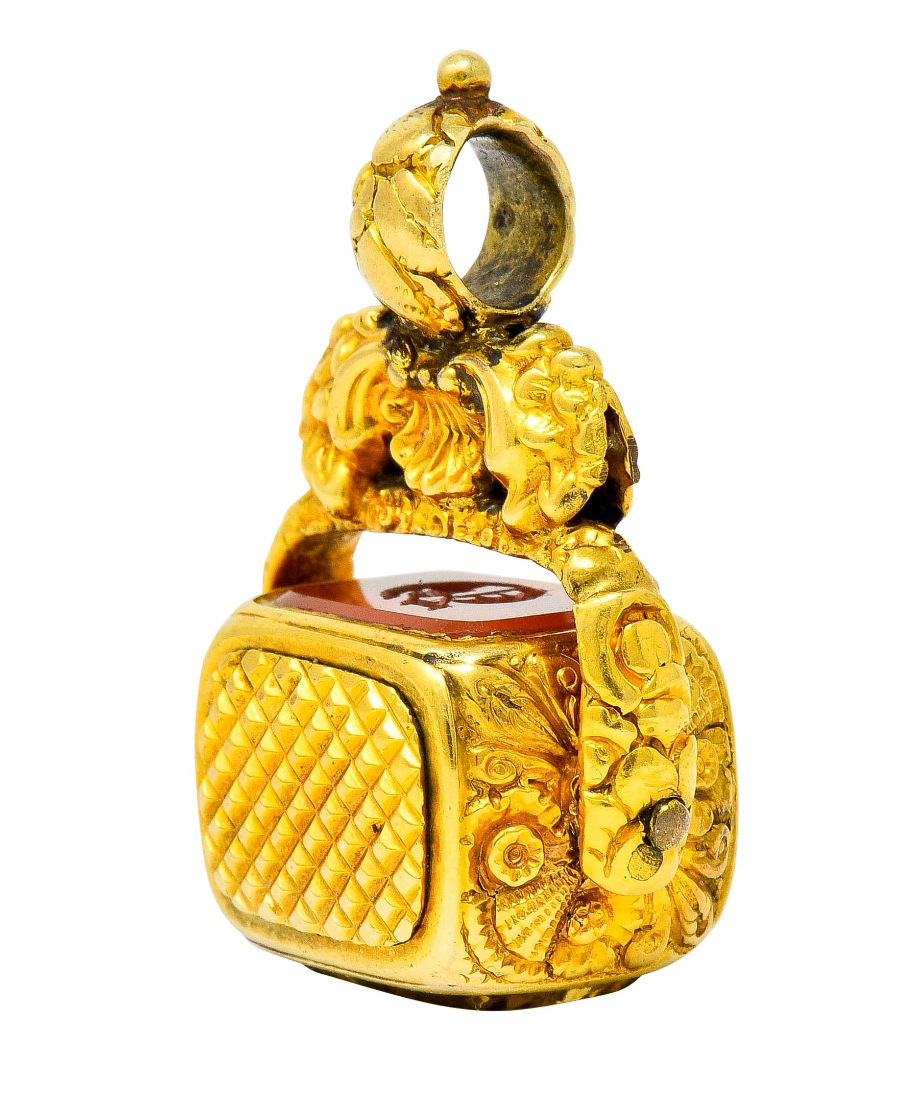 Fob pendant is designed with a stylized shell surmount with a looped floral bale topped by a polished gold bead

Suspending a gold frame decorated as a highly rendered floral motif that holds a rotating rectangular barrel form that has same floral