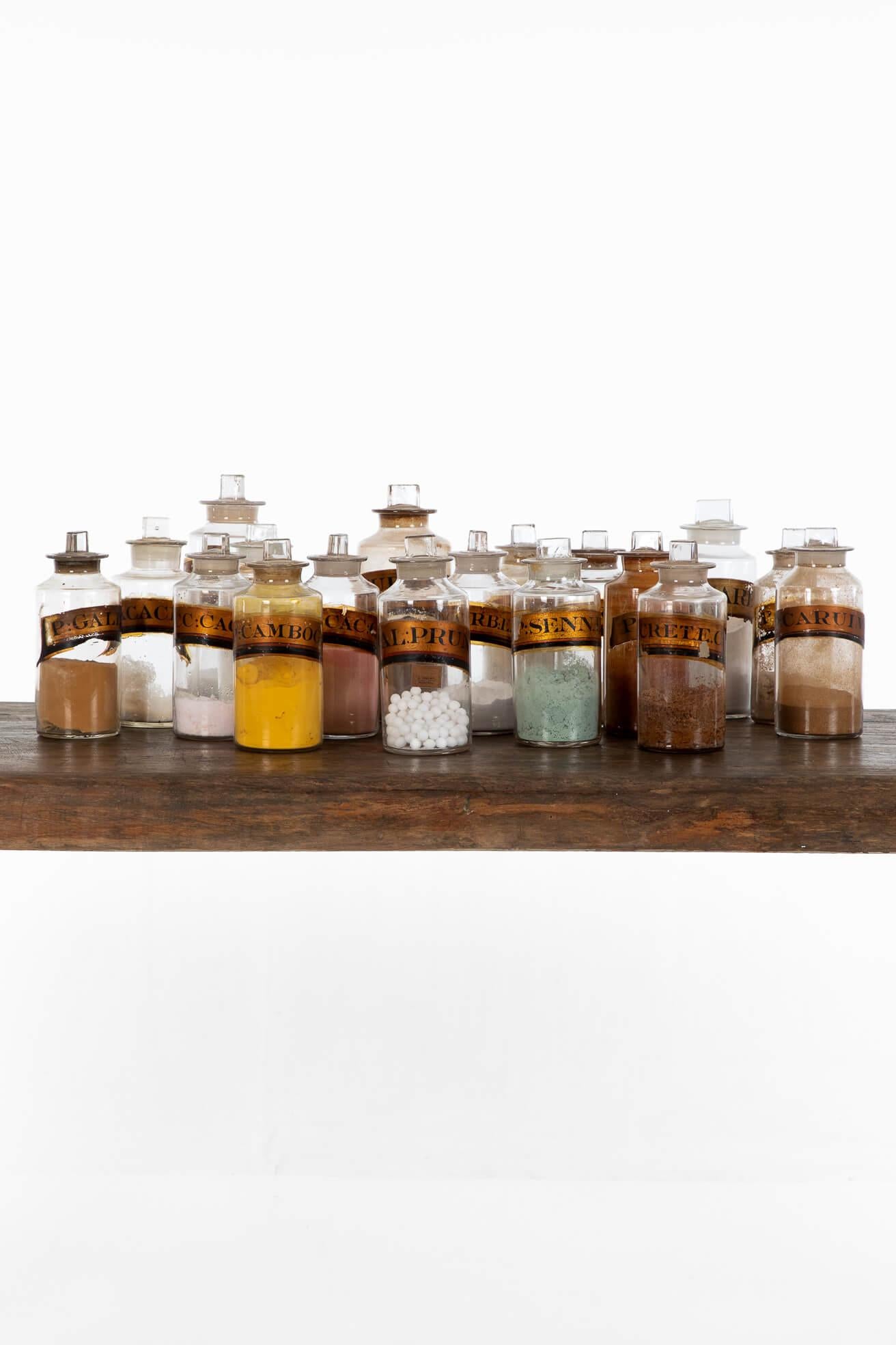 A collection of eighteen Georgian apothecary bottles from a British museum with original contents to each.

Each bottle features an original glass stopper over a gold leaf hand-painted label, written in Latin.

The three large and fifteen medium