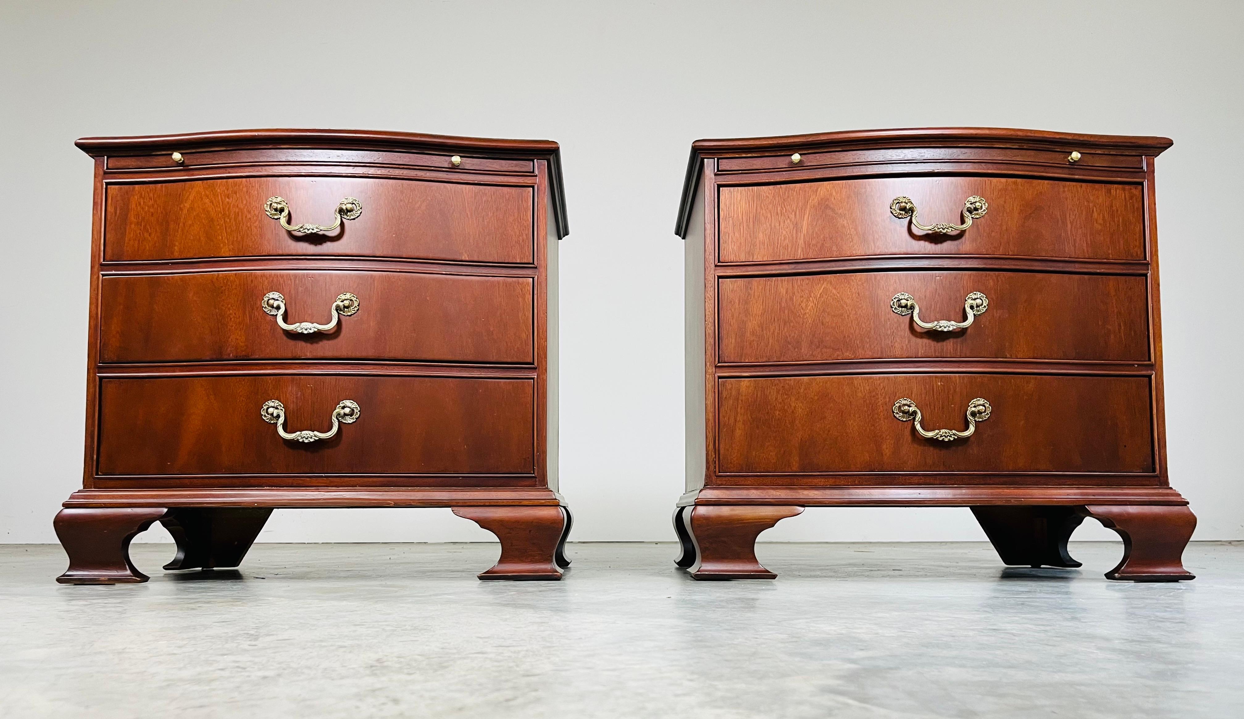 A pair of elegant Chippendale style nightstands by Baker Furniture Company in Mahogany with detailed solid brass pulls and oak interiors. Both nightstands feature 3 deep drawers with ample storage and an 8” pull-out tray at the top. In beautiful