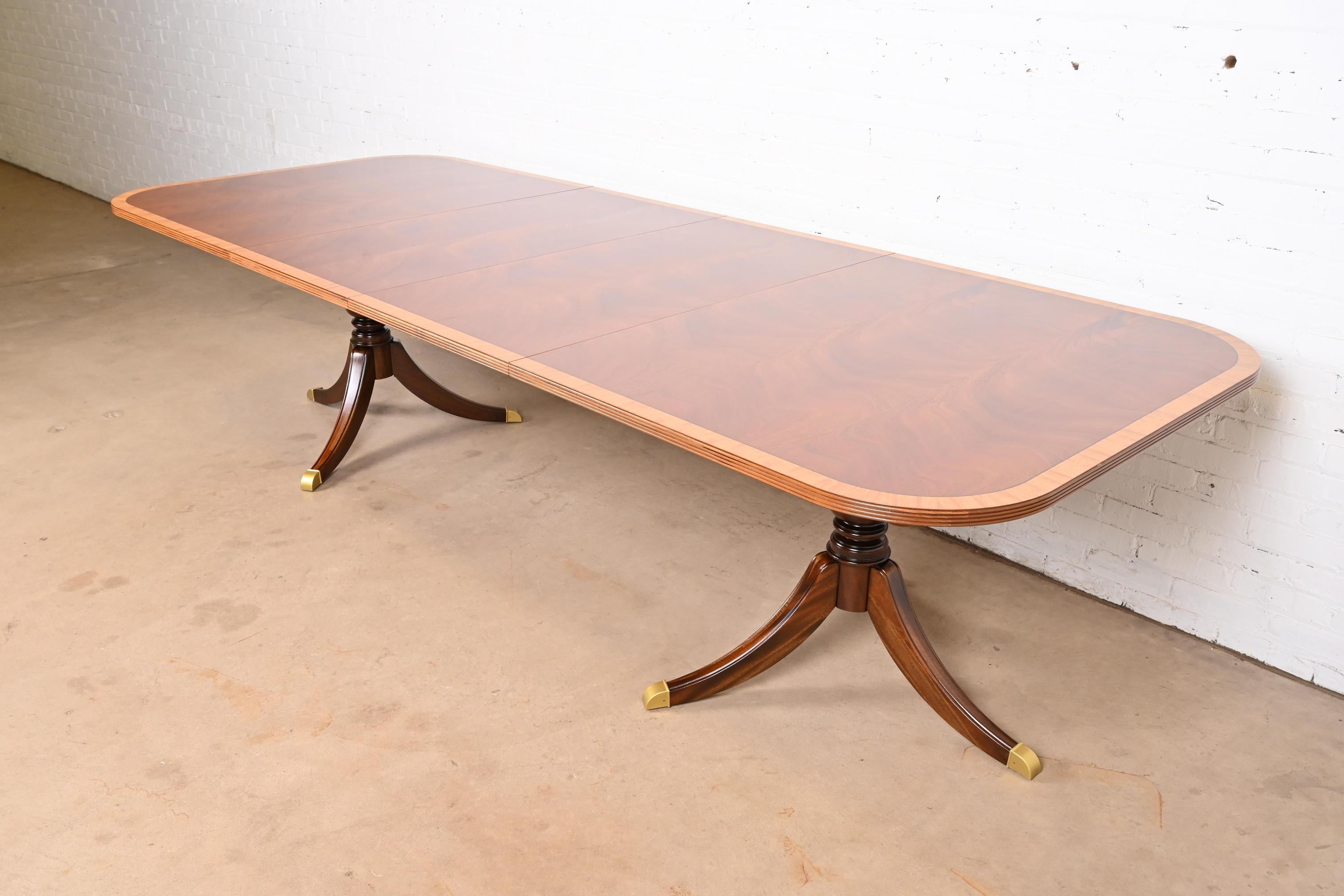 An exceptional Georgian or Regency style double pedestal extension dining table

USA, Late 20th Century

Gorgeous book-matched flame mahogany, with satinwood banding, carved solid mahogany pedestals, and brass-capped feet.

Measures: 74