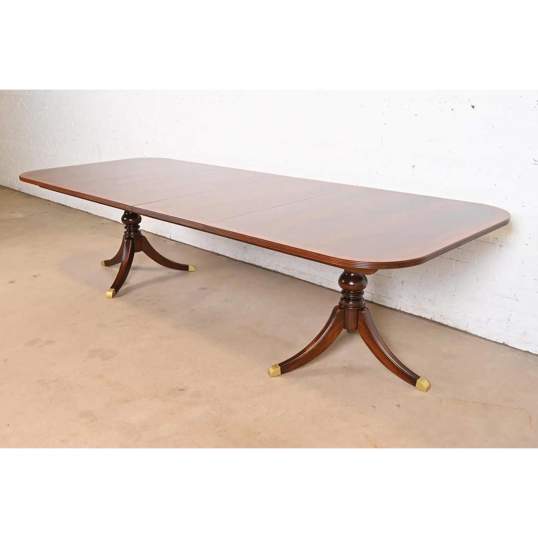 An exceptional Georgian or Regency style double pedestal extension dining table

USA, Late 20th Century

Gorgeous book-matched flame mahogany, with satinwood banding, carved solid mahogany pedestals, and brass-capped feet.

Measures: 74
