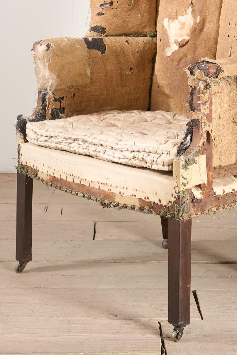 Se trata de un fabuloso sillón georgiano del siglo XVIII con respaldo de barril. Se alza sobre altas patas delanteras cuadradas con pequeñas ruedas de latón de época. La pata trasera tiene una reparación antigua bien hecha y es perfectamente sólida.